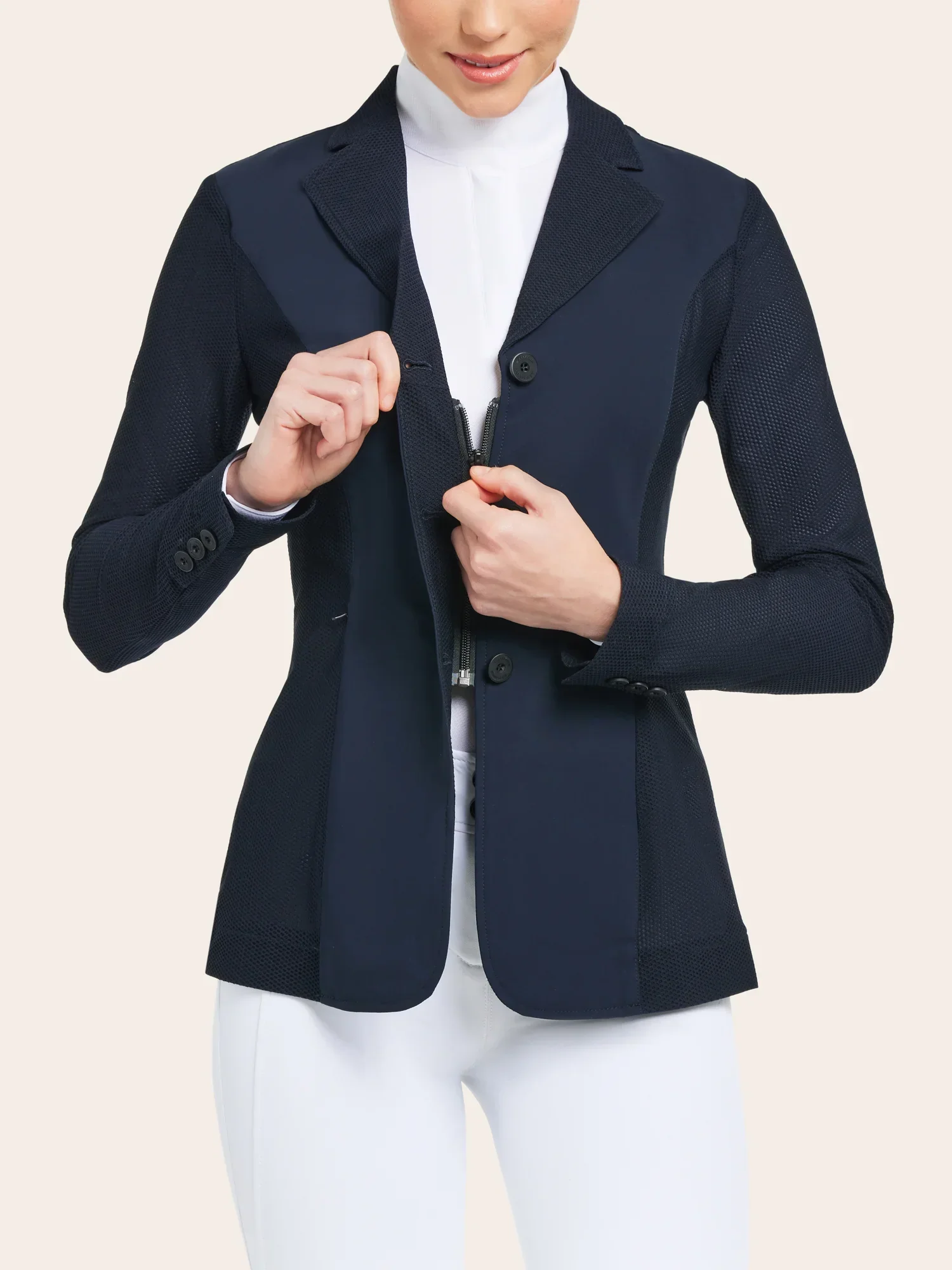 A woman is shown from the neck down, wearing a navy blue blazer with mesh panels and a white turtleneck, holding the lapel of her blazer.