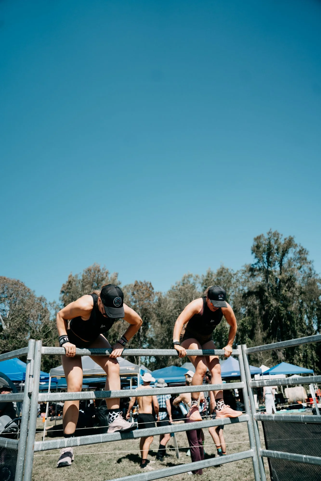 Two Farm Fit competitors climbing over a steel farm gate under a big blue sky at The Farm Jam, Tocal College