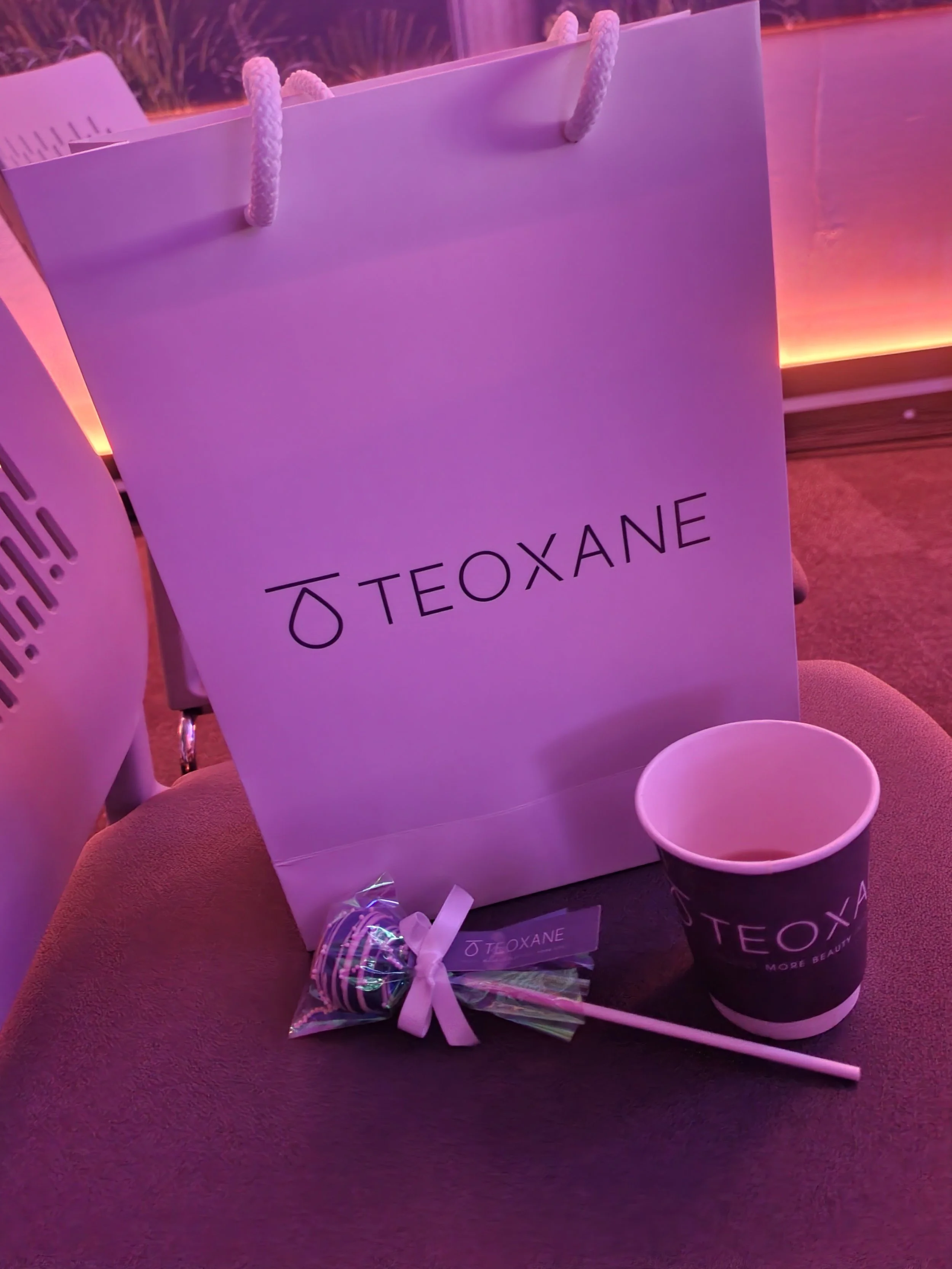 TEOXANE shopping bag, cup, and a lollipop on a seat, with purple lighting.