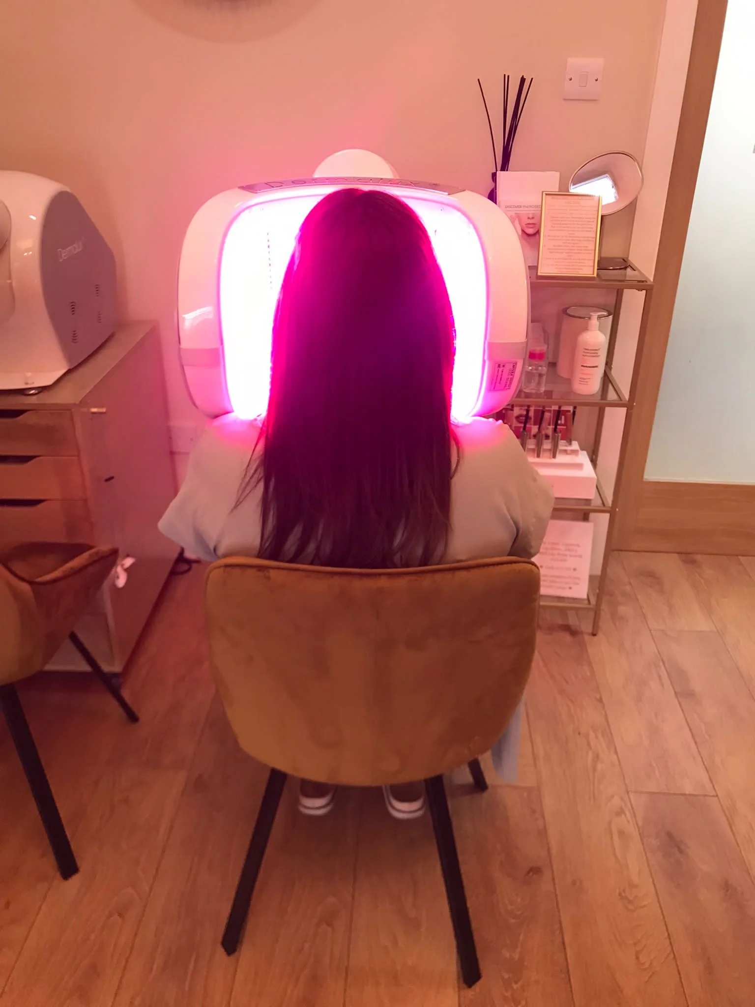 A woman with long dark hair sitting in front of a tanning bed with bright pink light.