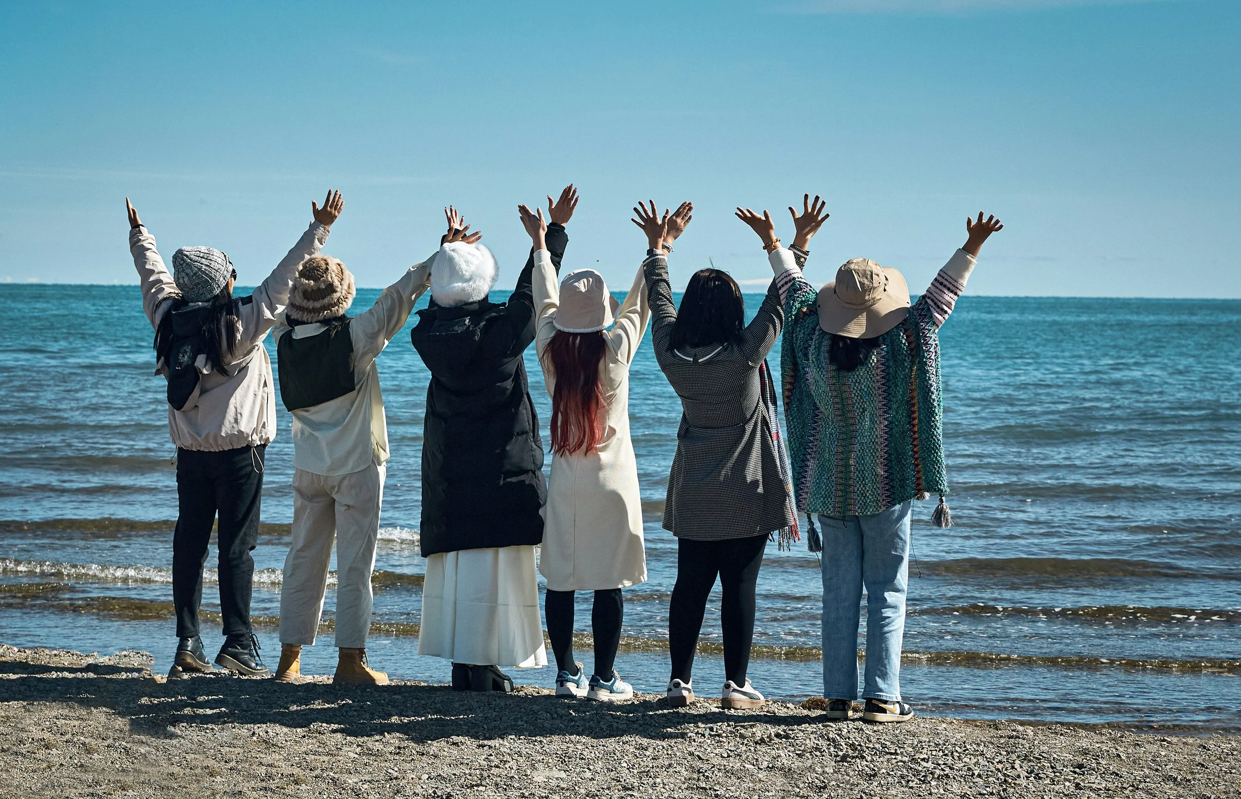 A group of friends celebrating on a scenic coastline with arms raised, representing professionally planned group travel and milestone celebration trips by The Unpunctual.