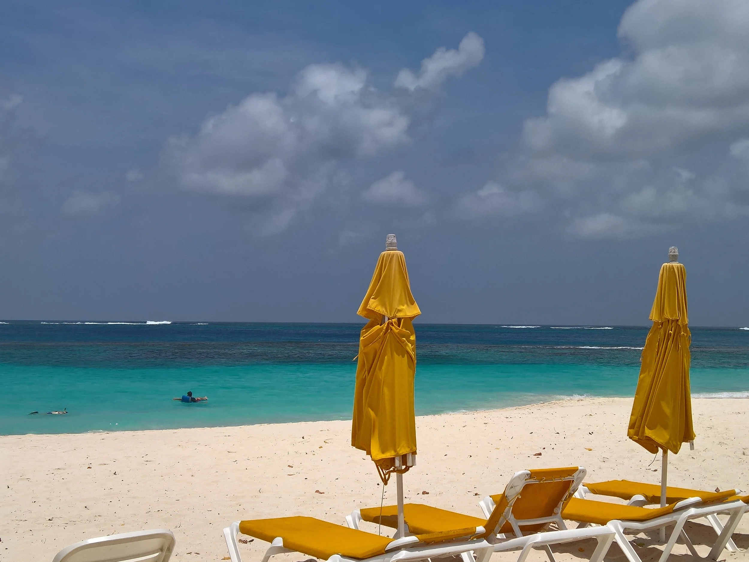 Yellow beach umbrellas on the white sands of Anguilla, representing tailored Caribbean island-hopping itineraries and exclusive multi-destination trip vacations.