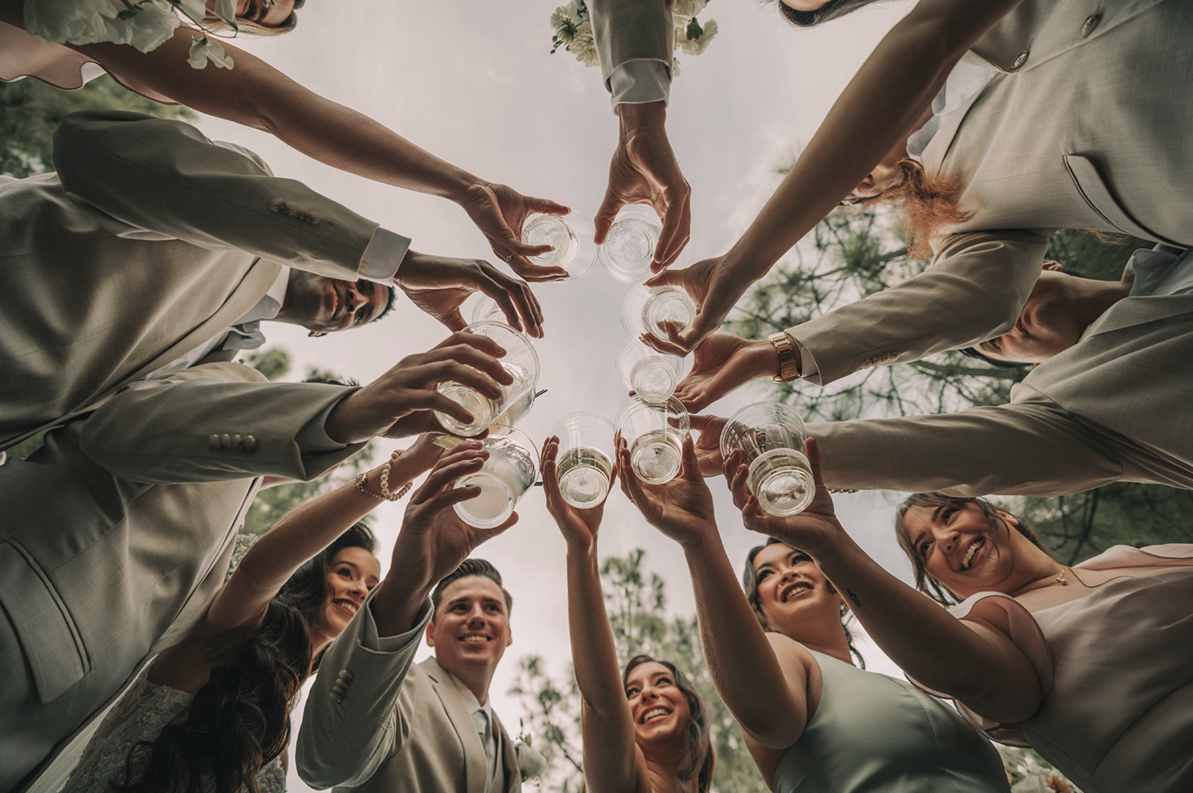 Group of people in formal attire raising glasses for a toast at an outdoor event, smiling and celebrating under cloudy sky. Wedgewood wedding venue Chino Hills.