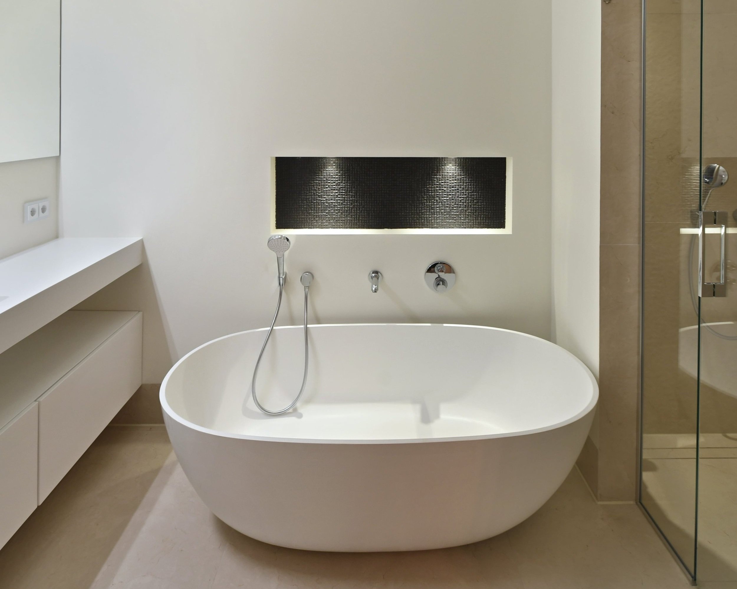 Moderne witte vrijstaande badkuip in een minimalistische badkamer met zwarte waterspiegel en inloopdouche.