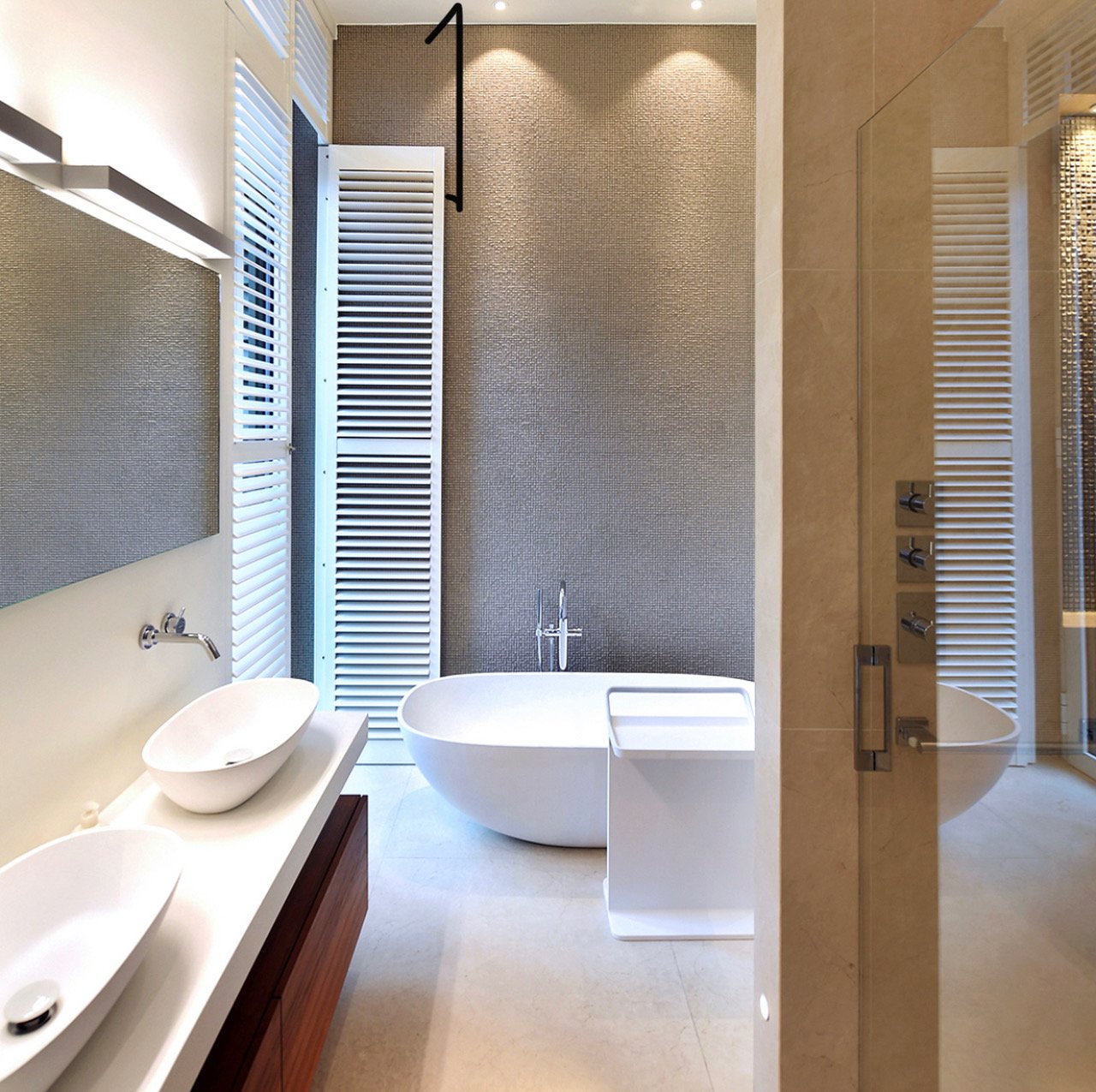 Luxe badkamer met vrijstaande badkuip, dubbele wastafels, spiegel, verwarming, douche met glazen deur, en natuurlijke lichtinval.