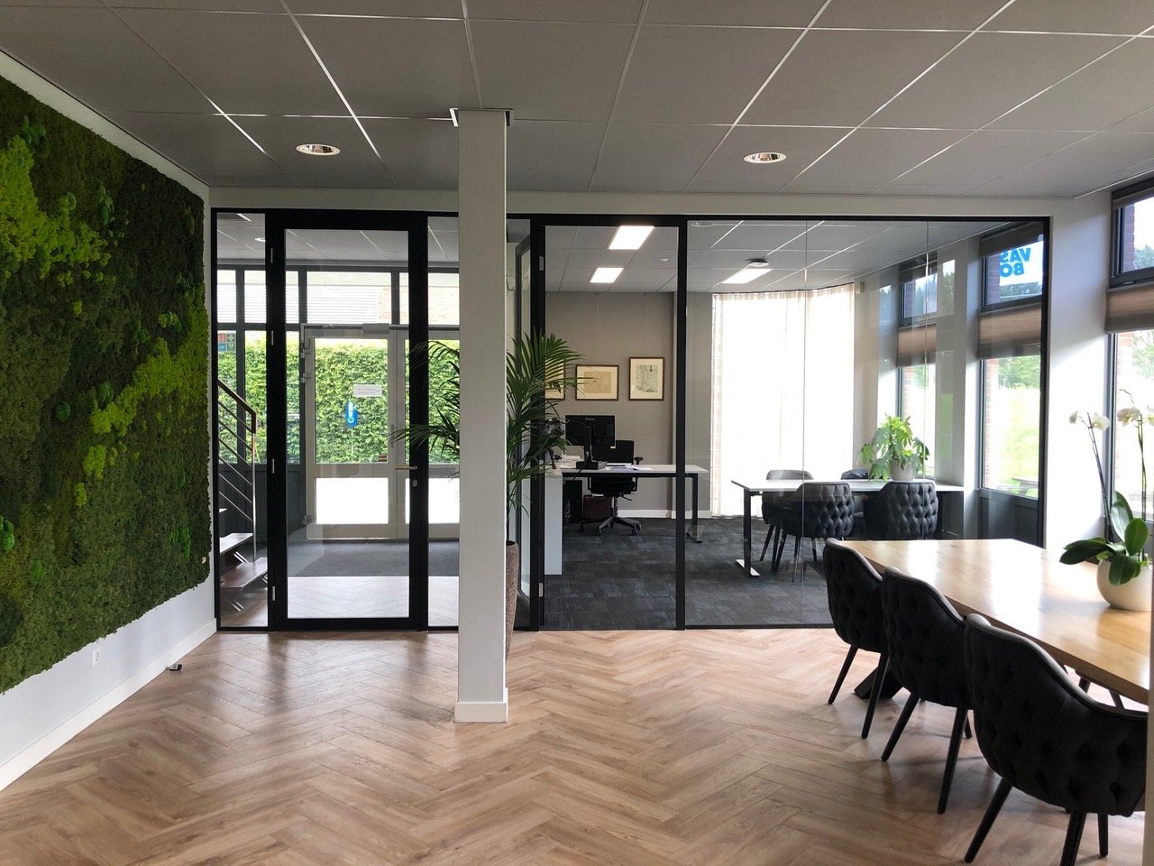 Modern kantoorruimte met houten vloer, groene muur en glazen wanden met kantoor- en vergaderruimtes.
