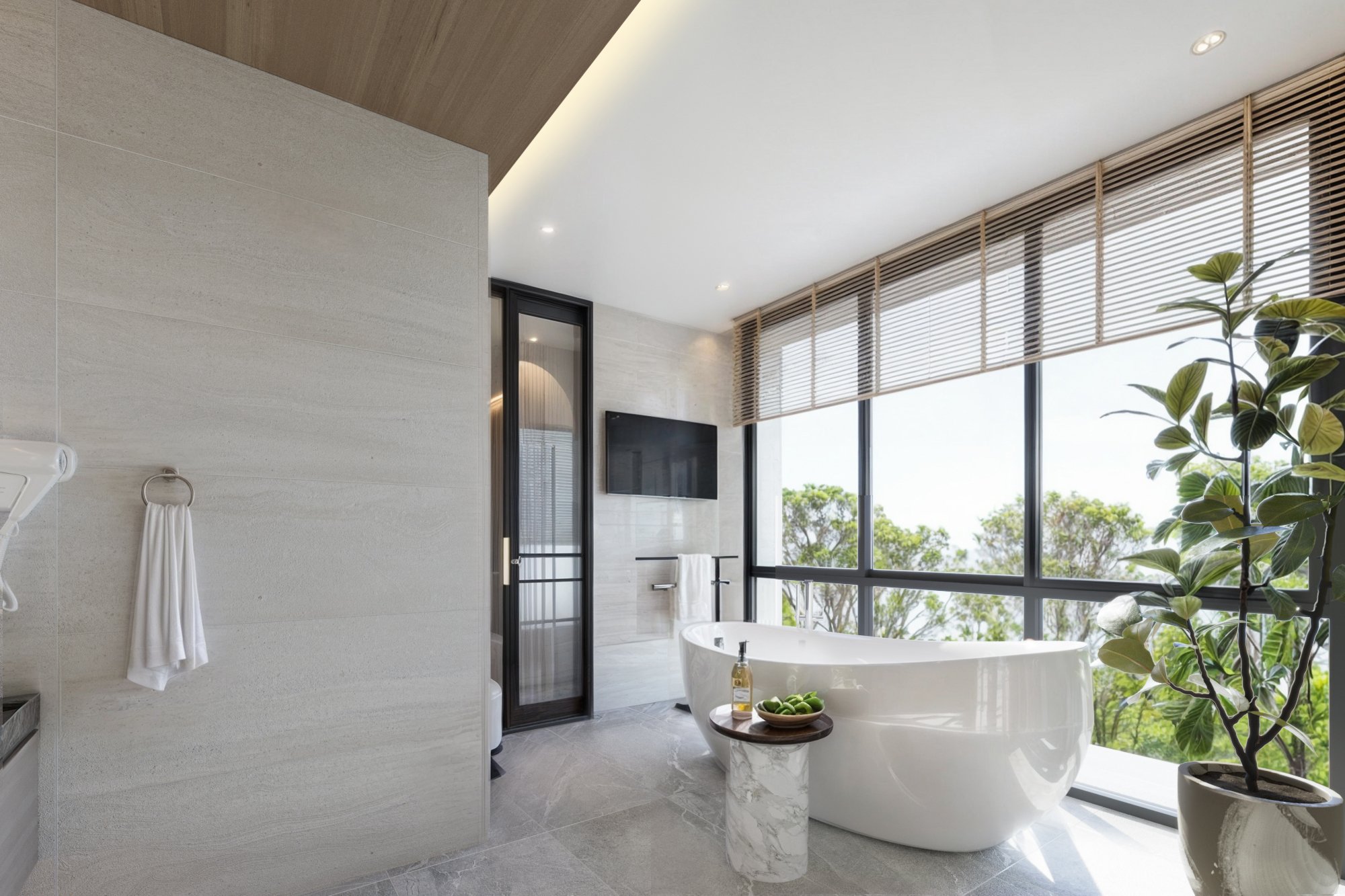 Modern bathroom with freestanding tub positioned near full-height windows overlooking greenery.