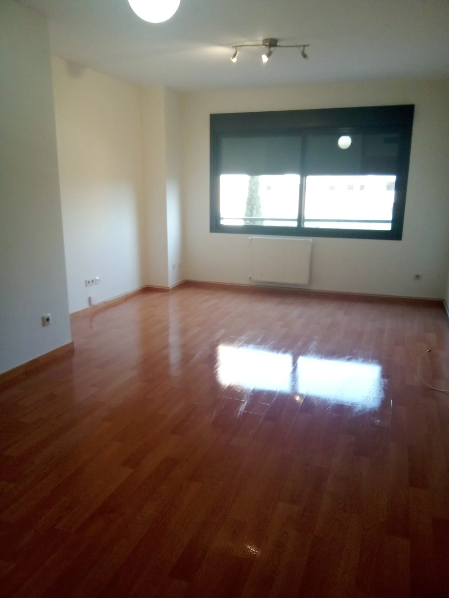 Sala vacía con ventanas y suelo de madera pulida.