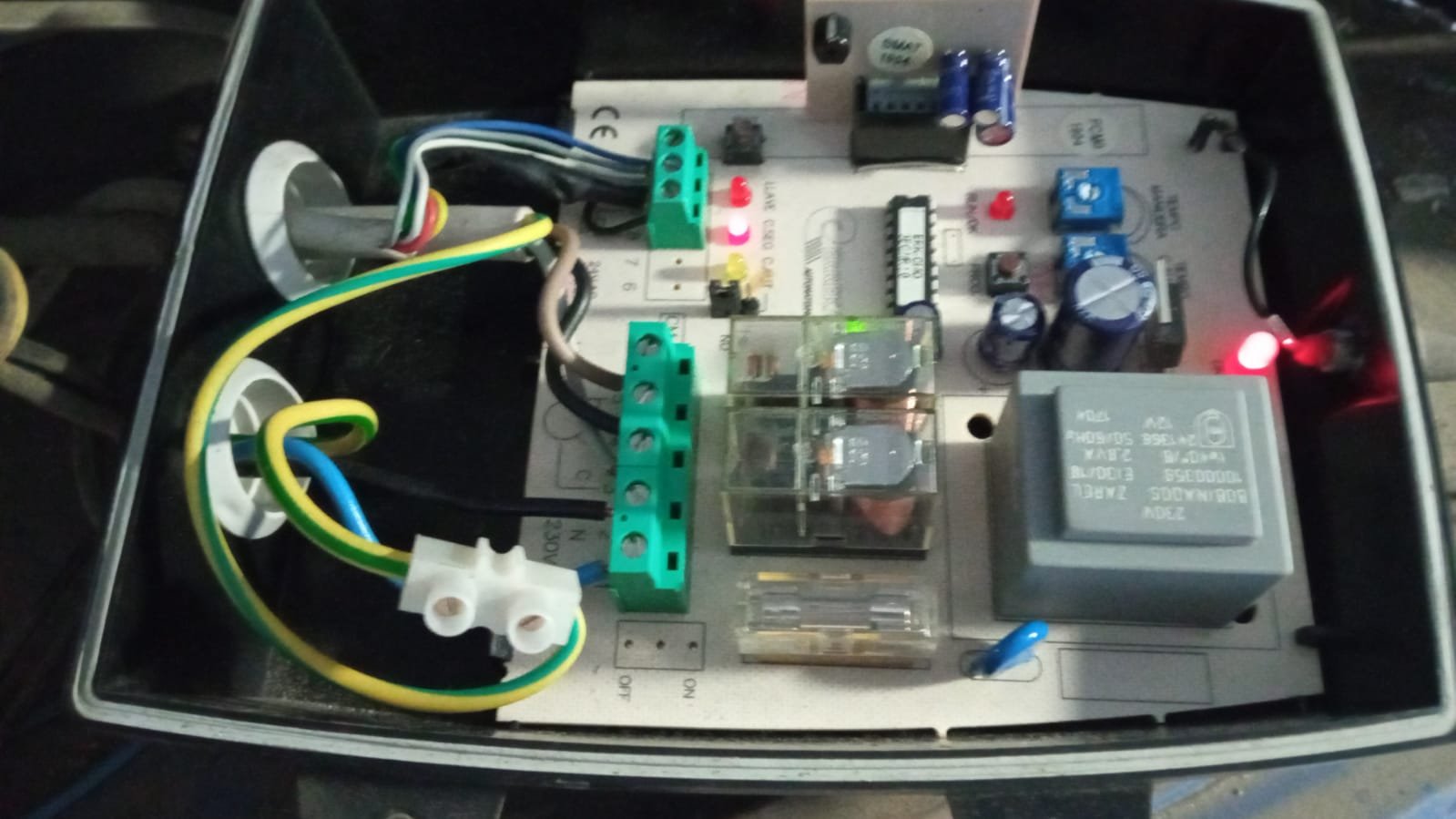 Circuito electrónico con componentes como relés, condensadores, resistencias y conexiones de cables en una caja de metal.