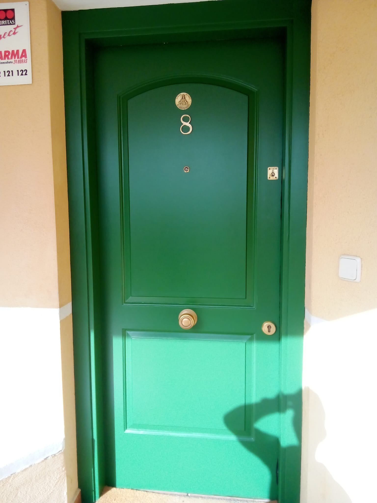 Puerta verde con el número 8 y una placa con una imagen en la parte superior, ubicada en una pared beige.