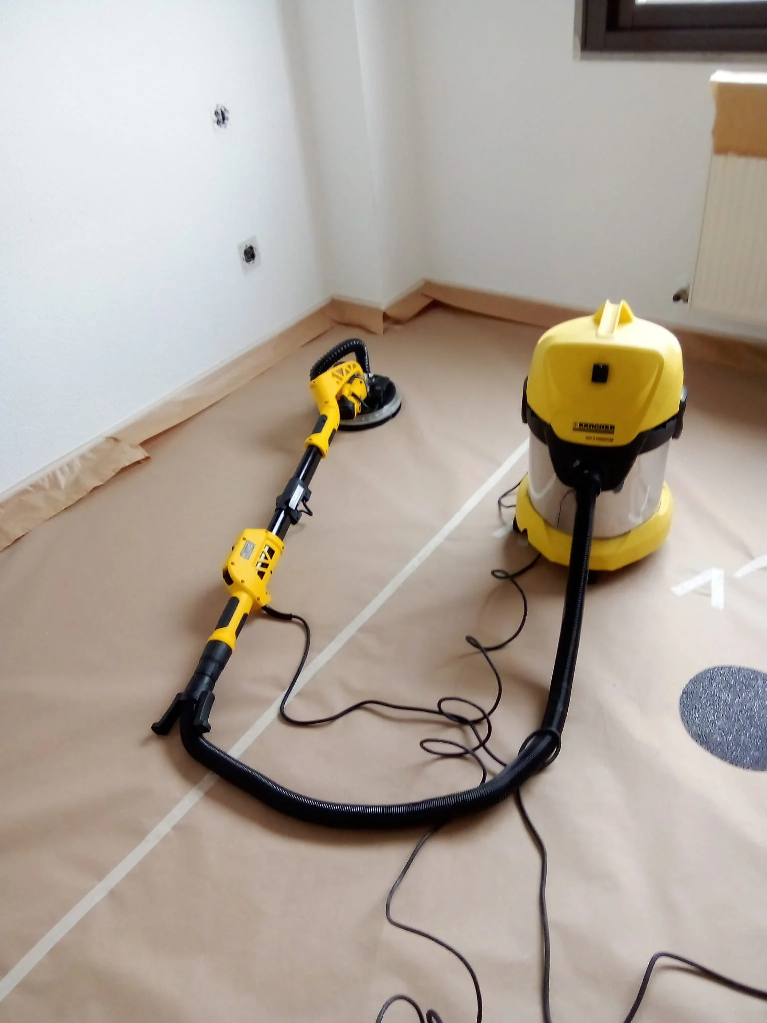 Tira papel protector en la habitación, que contiene una aspiradora amarilla y negra y un atomizador de mano amarillo, para limpieza o renovación de pintura.