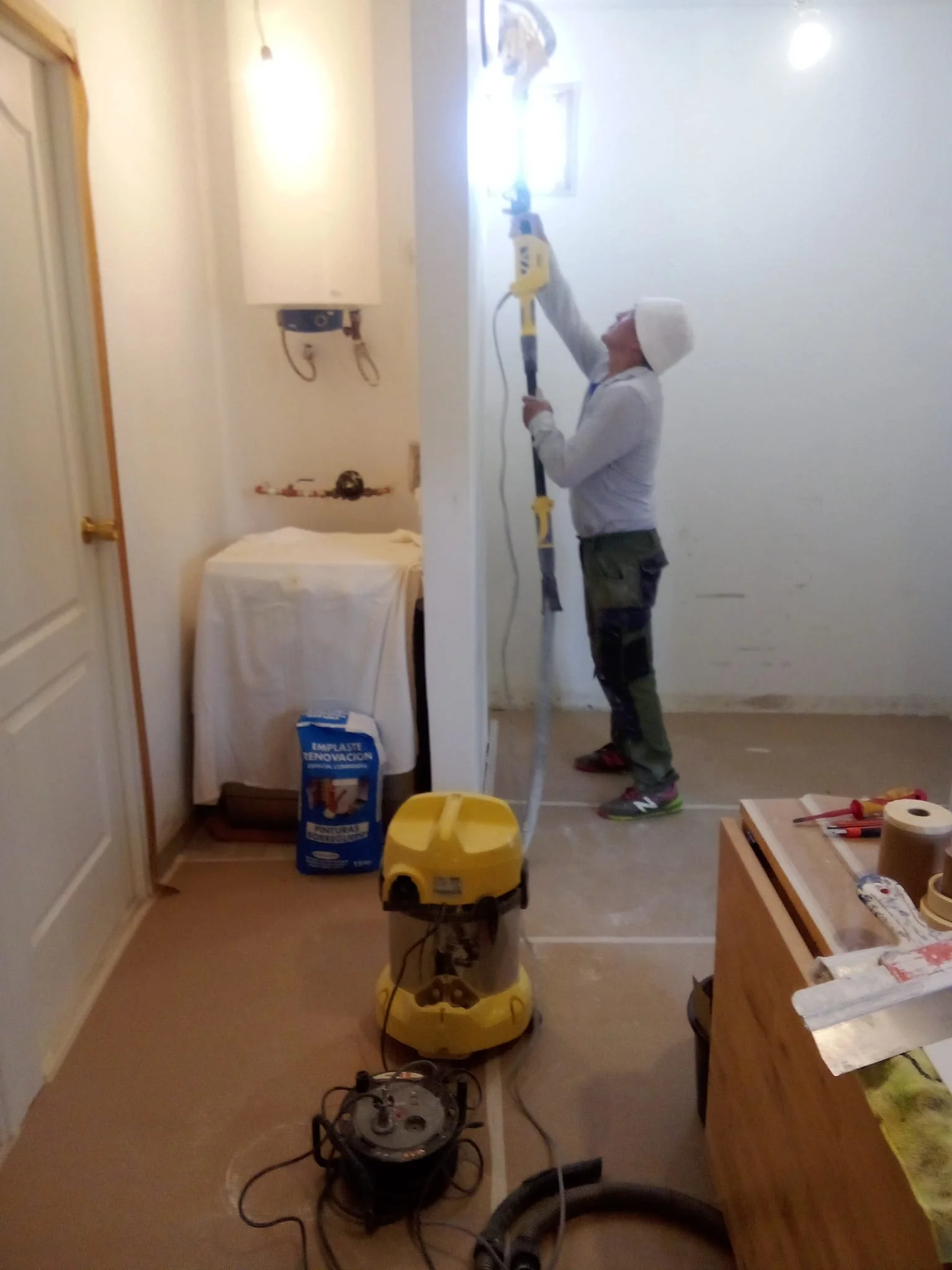 Persona trabajando en reparaciones eléctricas en interior de vivienda con herramientas y equipo de protección.