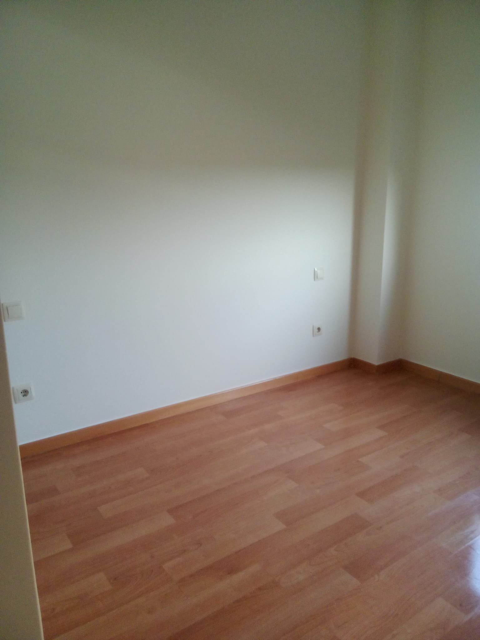 Una habitación vacía con paredes blancas, piso de madera y varias tomas eléctricas en la pared.
