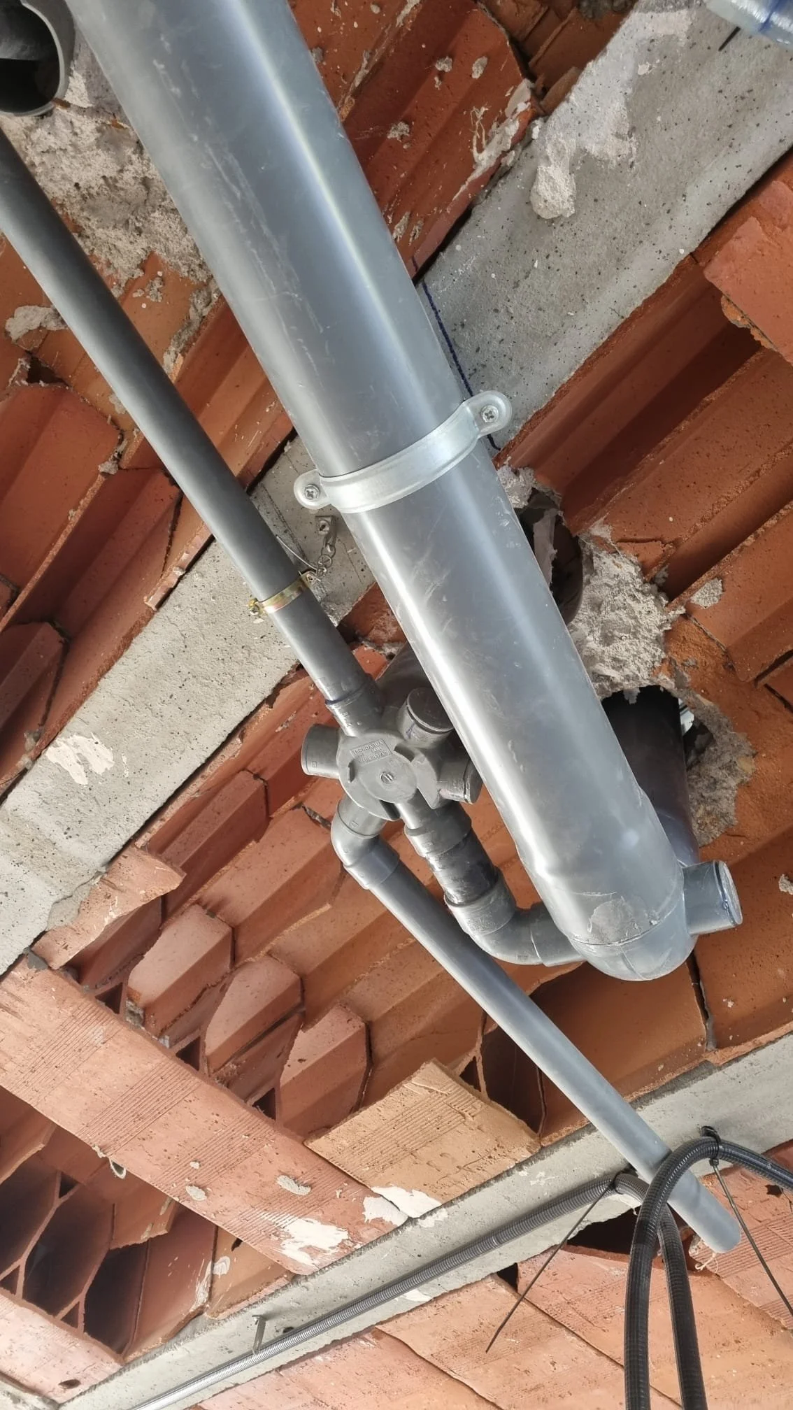Tubería de metal y conexiones en construcción, instalada en techo con ladrillos expuestos.
