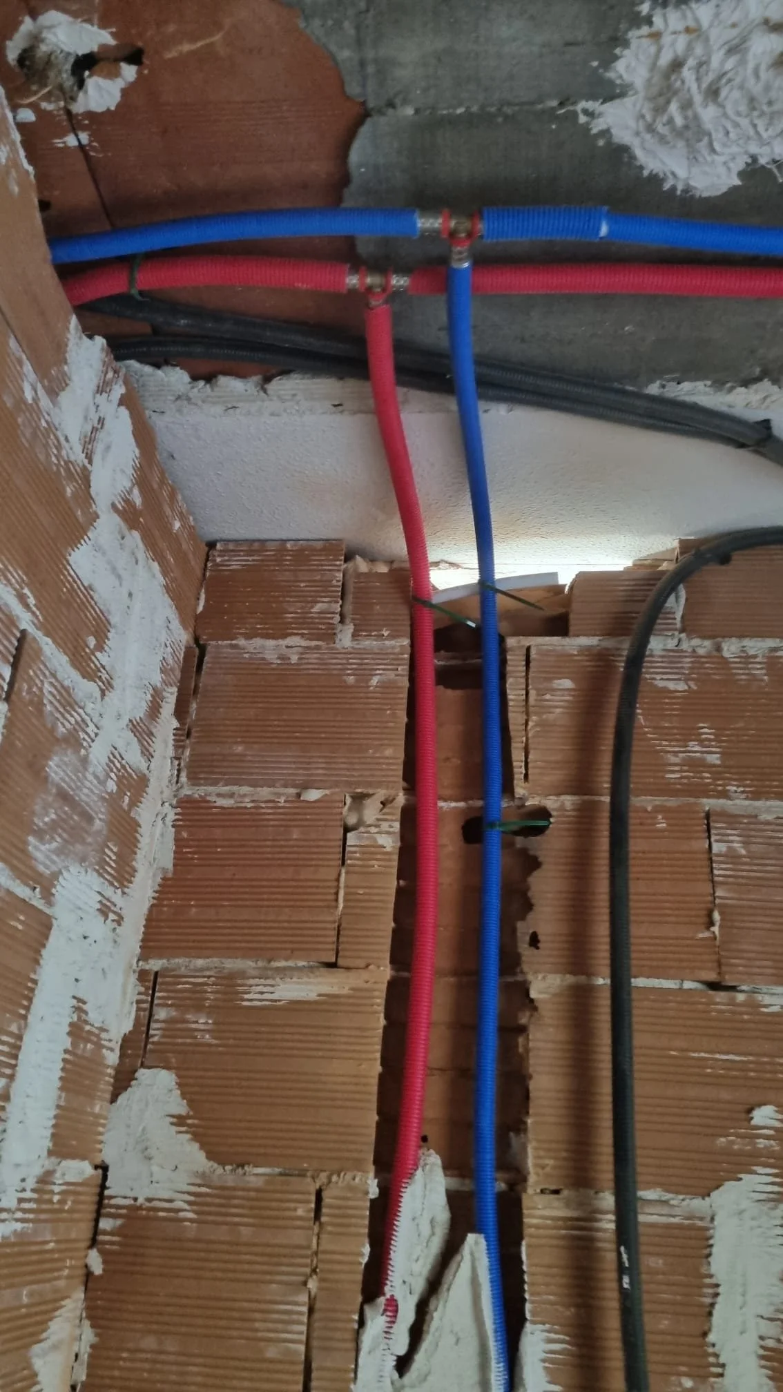 Tuberías de agua y cables eléctricos instalados en una pared de ladrillos en construcción