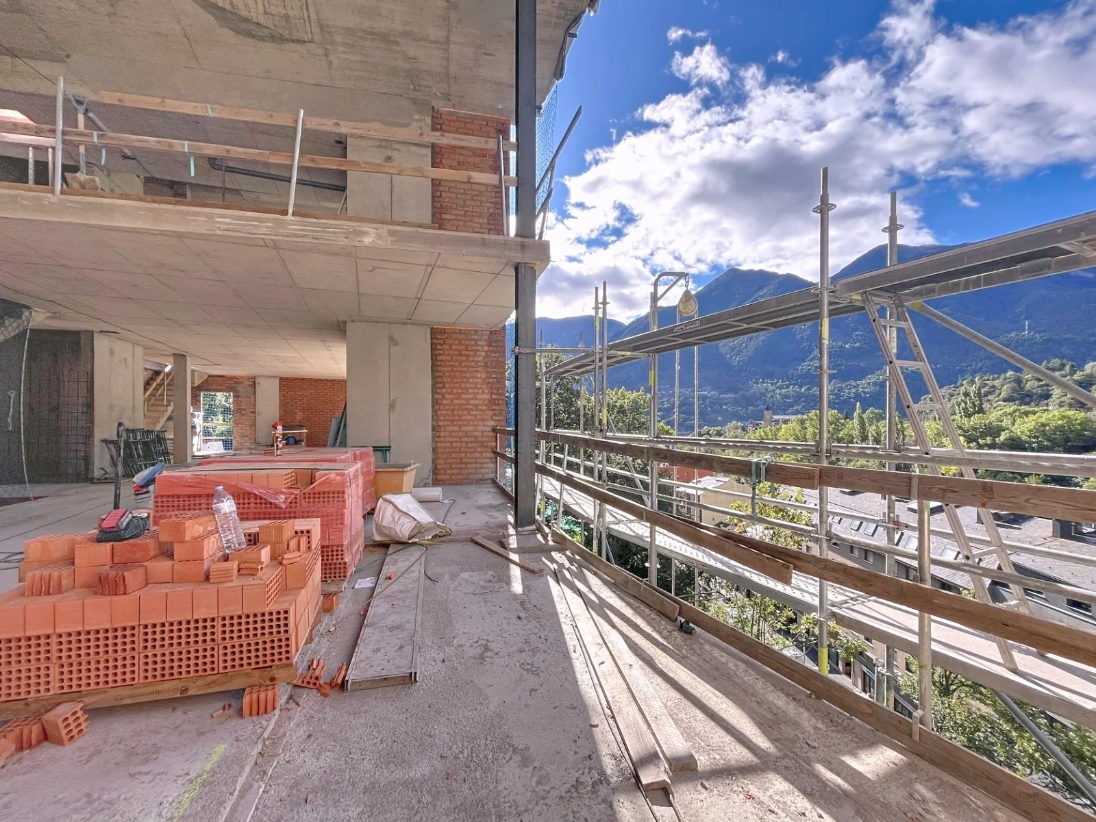 Construcción en progreso en un edificio con vista a las montañas y cielo con nubes, estructura de concreto y ladrillos, andamios y materiales de construcción en el sitio.