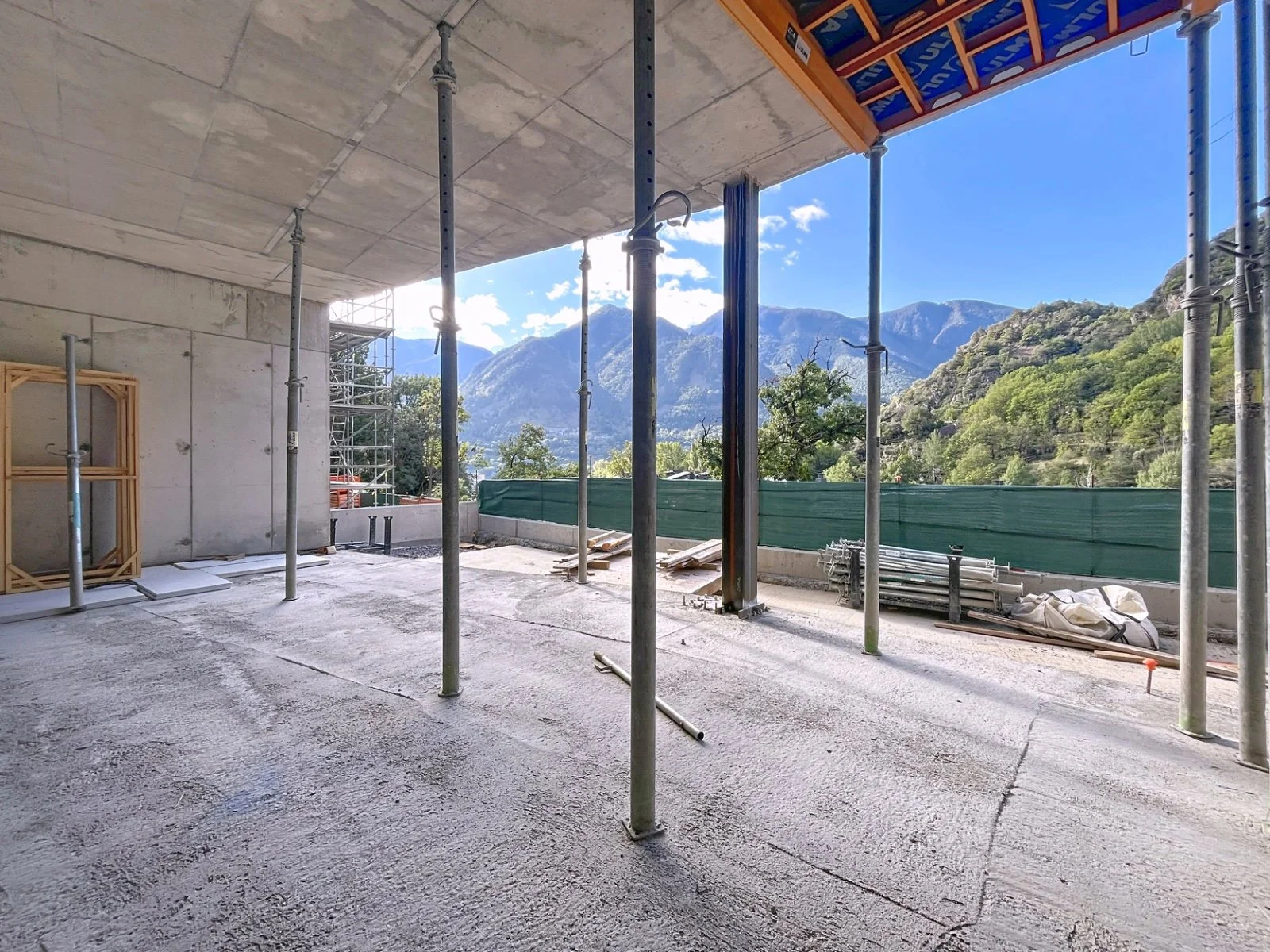 Estructura en construcción en un área con vista a montañas y árboles, con columnas de soporte y una cubierta de cemento.