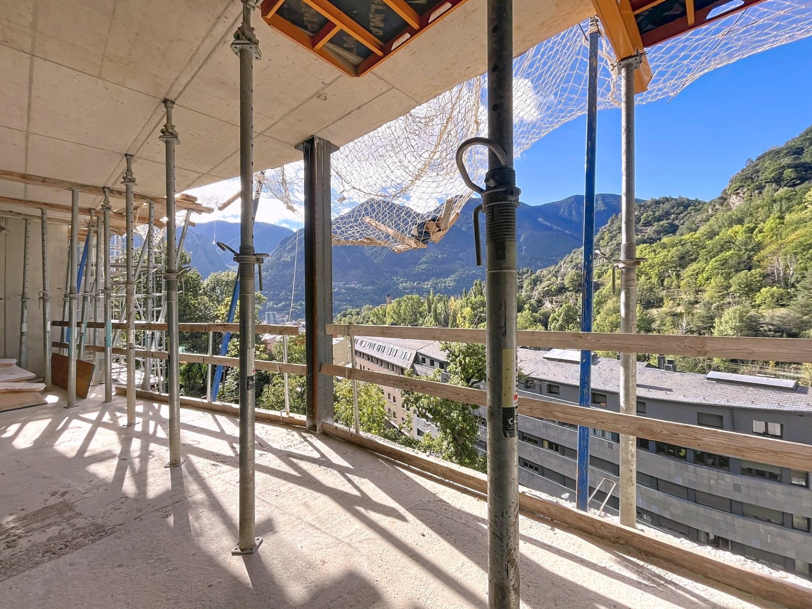 Construcción en un edificio alto con vistas a montañas y árboles, andamios y protección en el balcón.