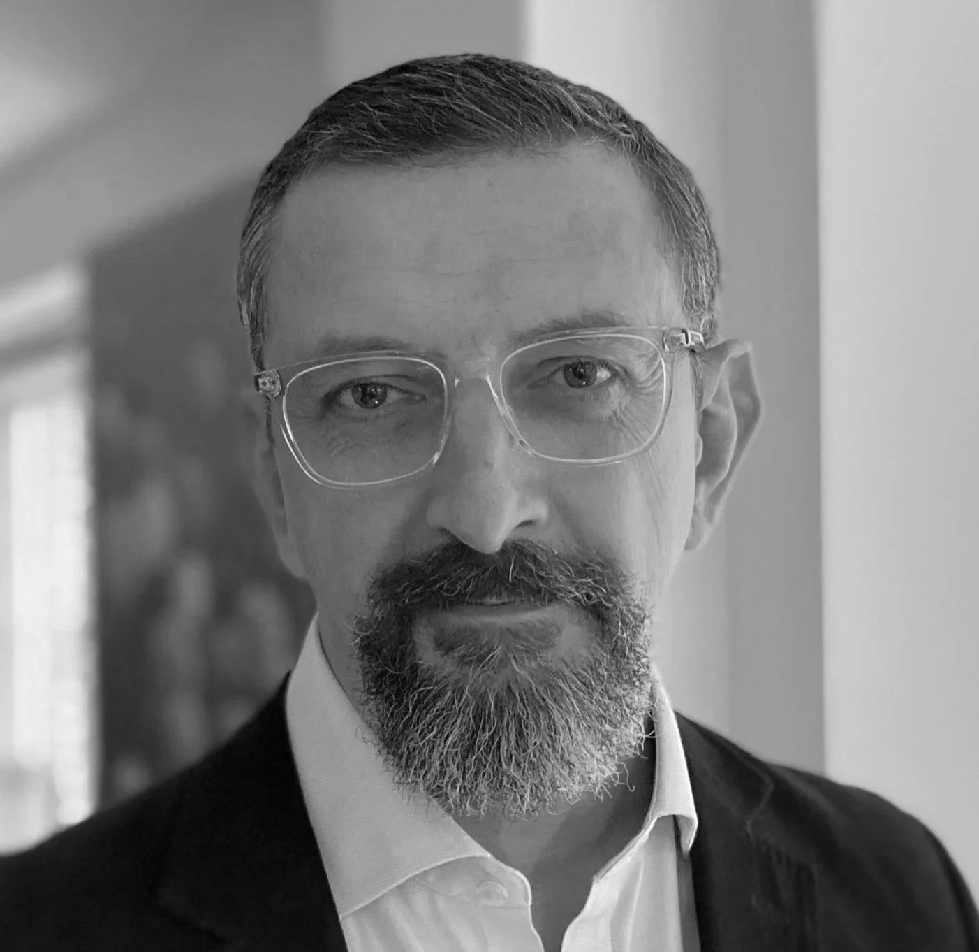 Black and white portrait of a middle-aged man with glasses, a beard, and a mustache, wearing a suit and white shirt, looking directly at the camera.