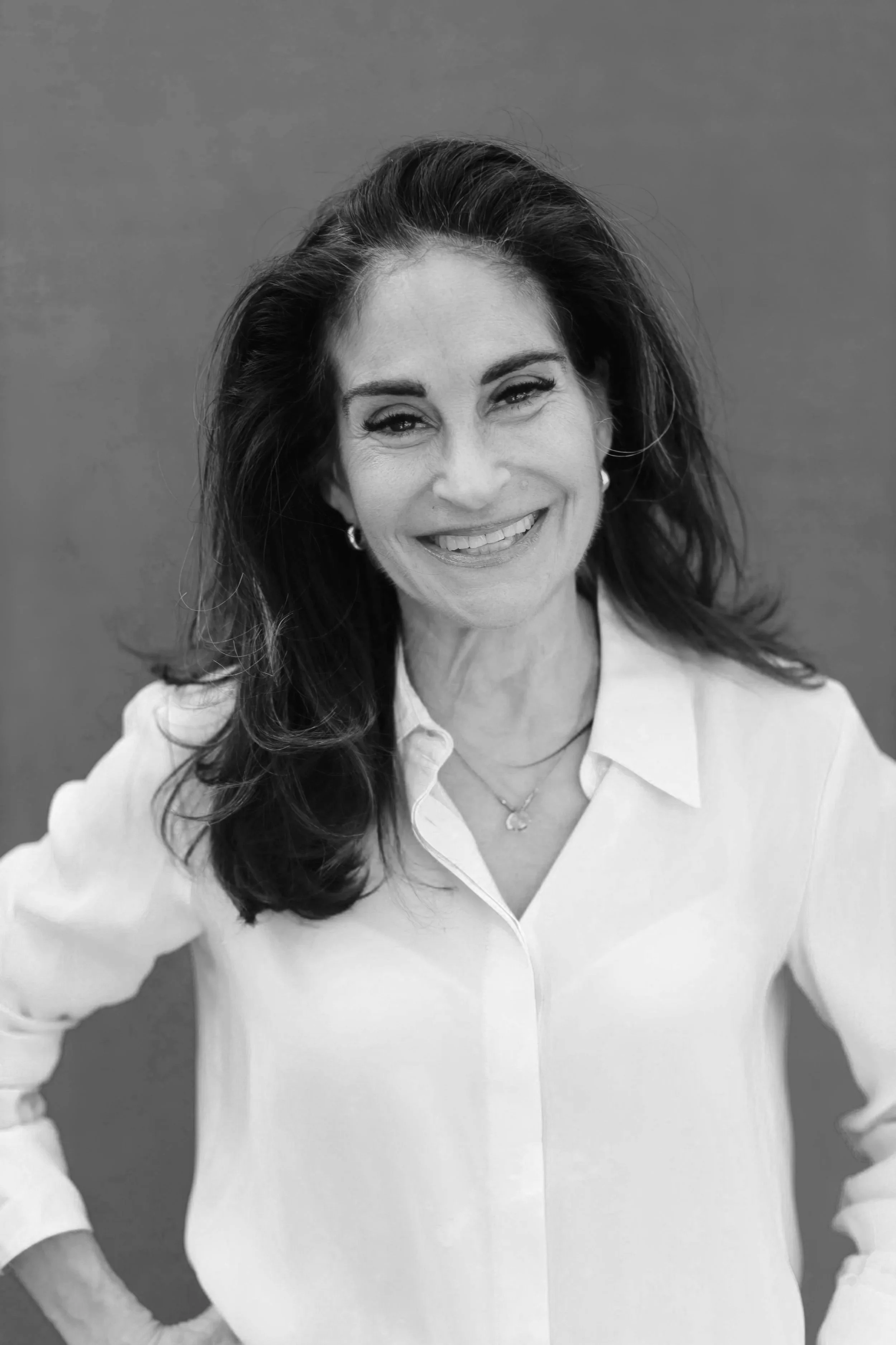 Susan McPherson A smiling woman with shoulder-length dark hair, wearing a white button-down shirt and jewelry, standing against a plain background.