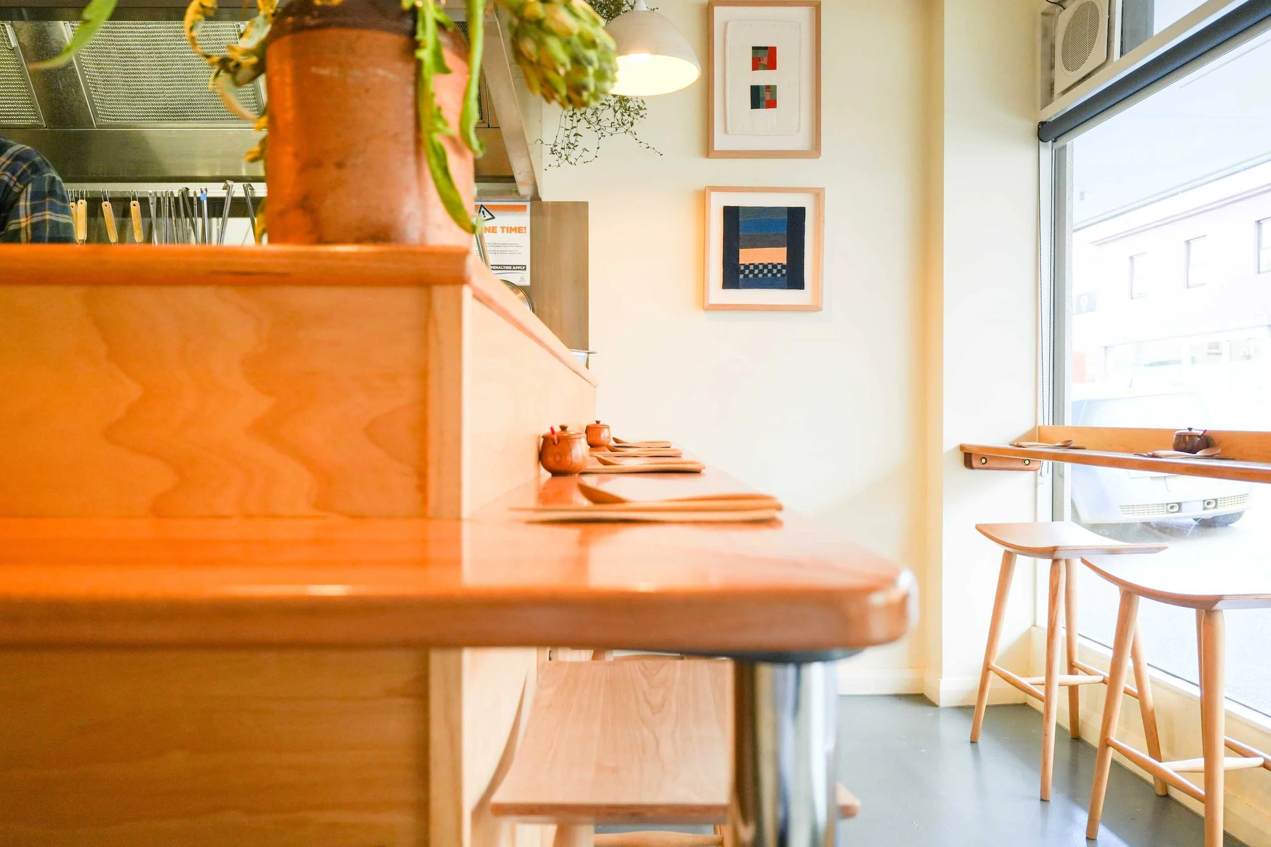 Compact ramen bar interior with light timber joinery, bench seating, and window-side stools, highlighting clean detailing and warm natural finishes
