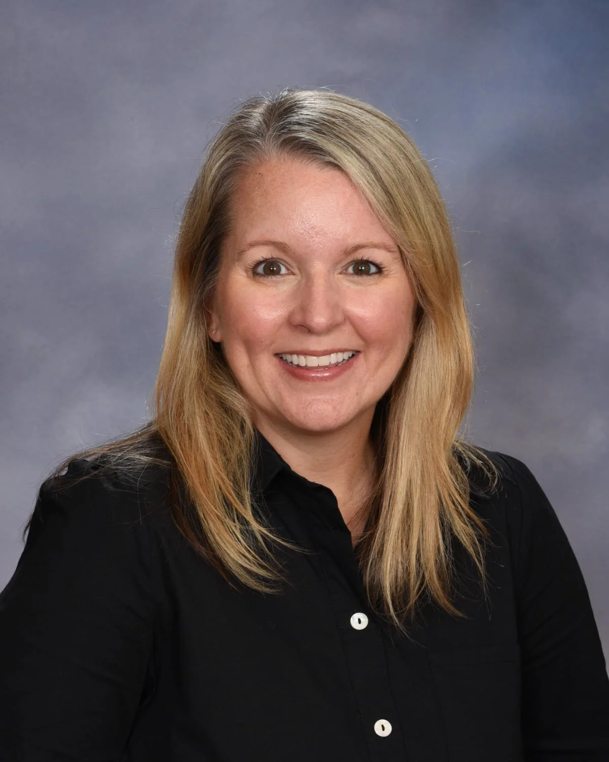 Portrait of a woman with shoulder-length blonde hair, wearing a black button-up shirt, smiling.