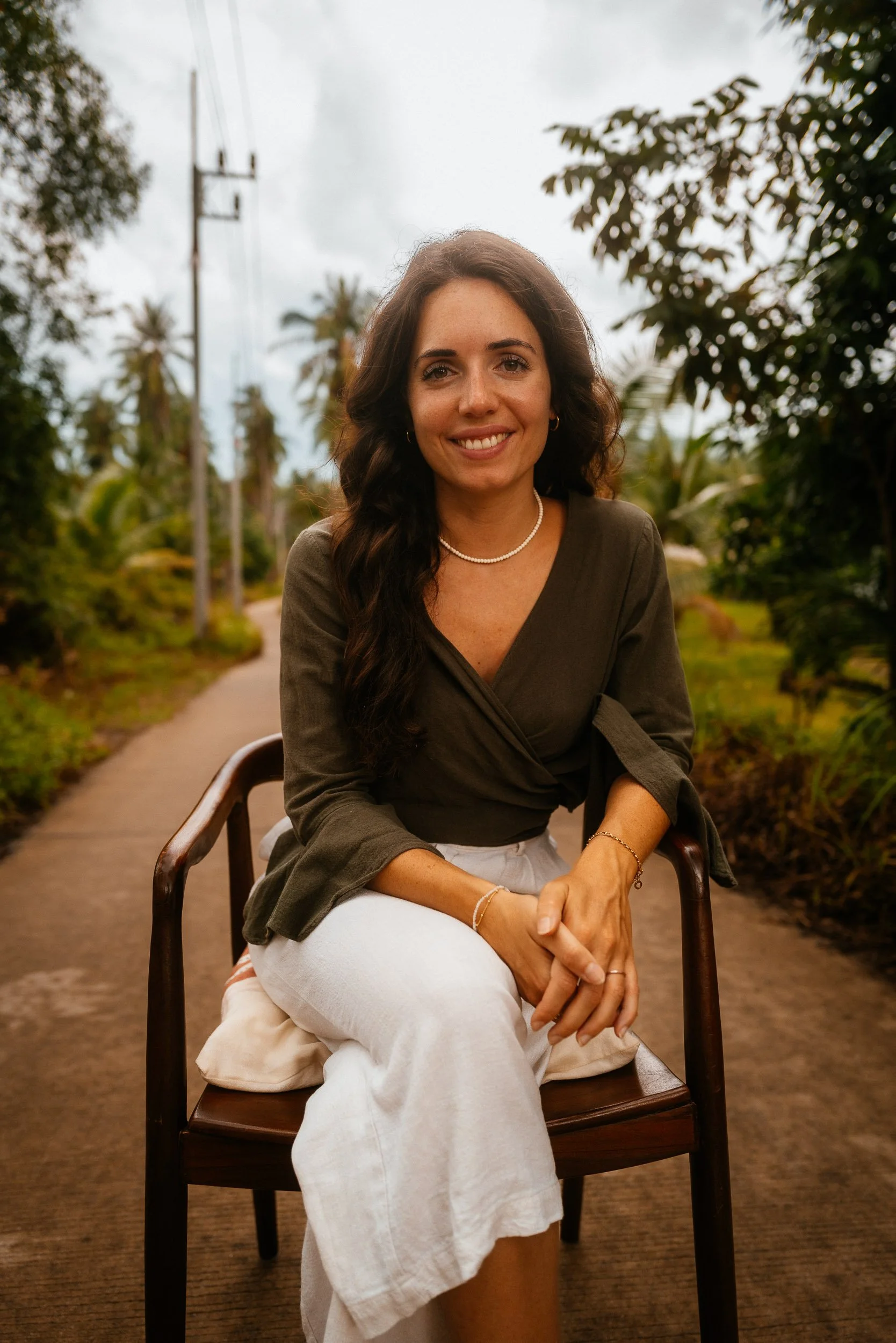 Eine lächelnde Frau sitzt auf einem Stuhl auf einem Pfad in einer grünen, bewölkten Natur.