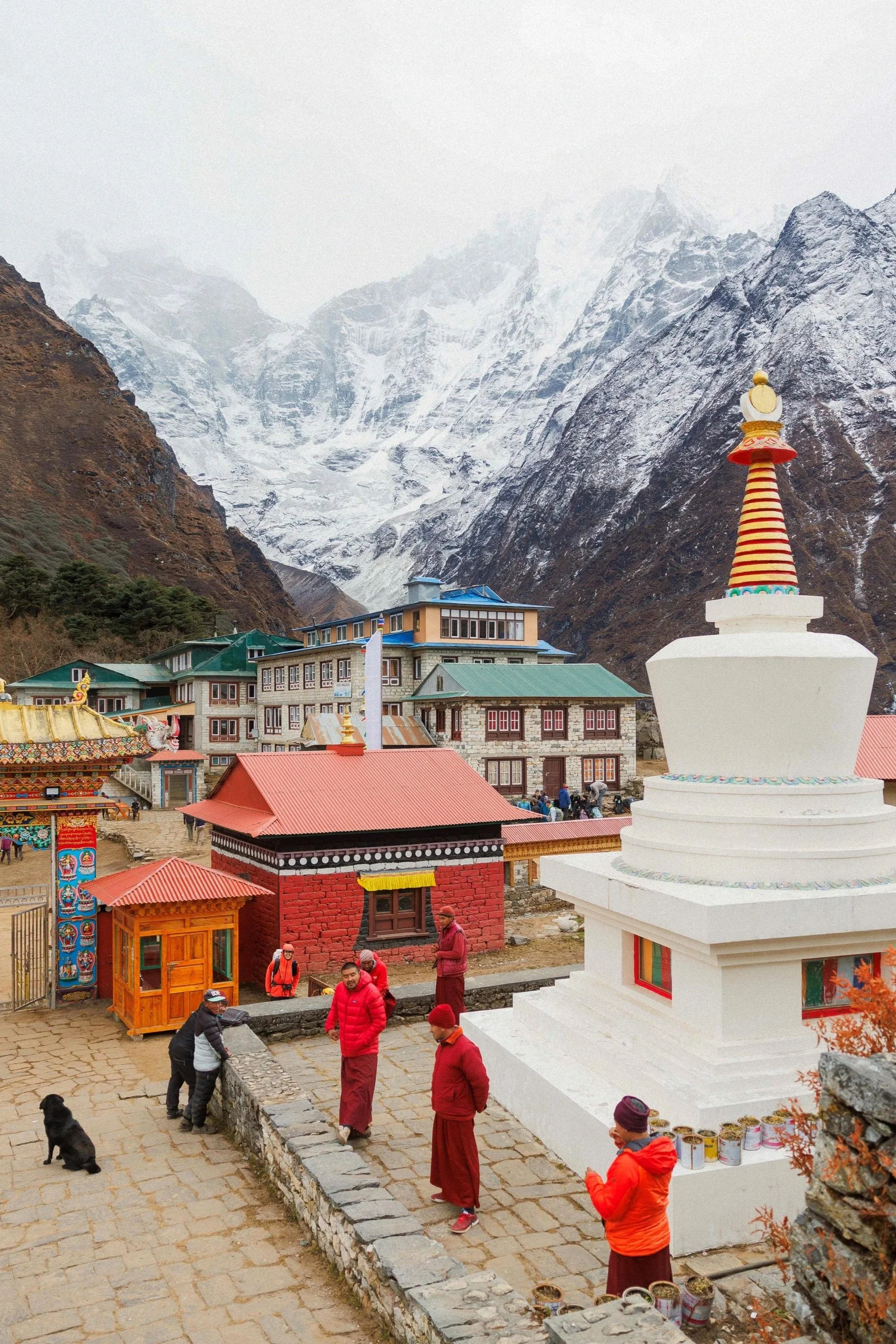 Buddhistisches Kloster in den Bergen mit Mönchen und Besuchern, umgeben von Schnee bedeckten Gipfeln.