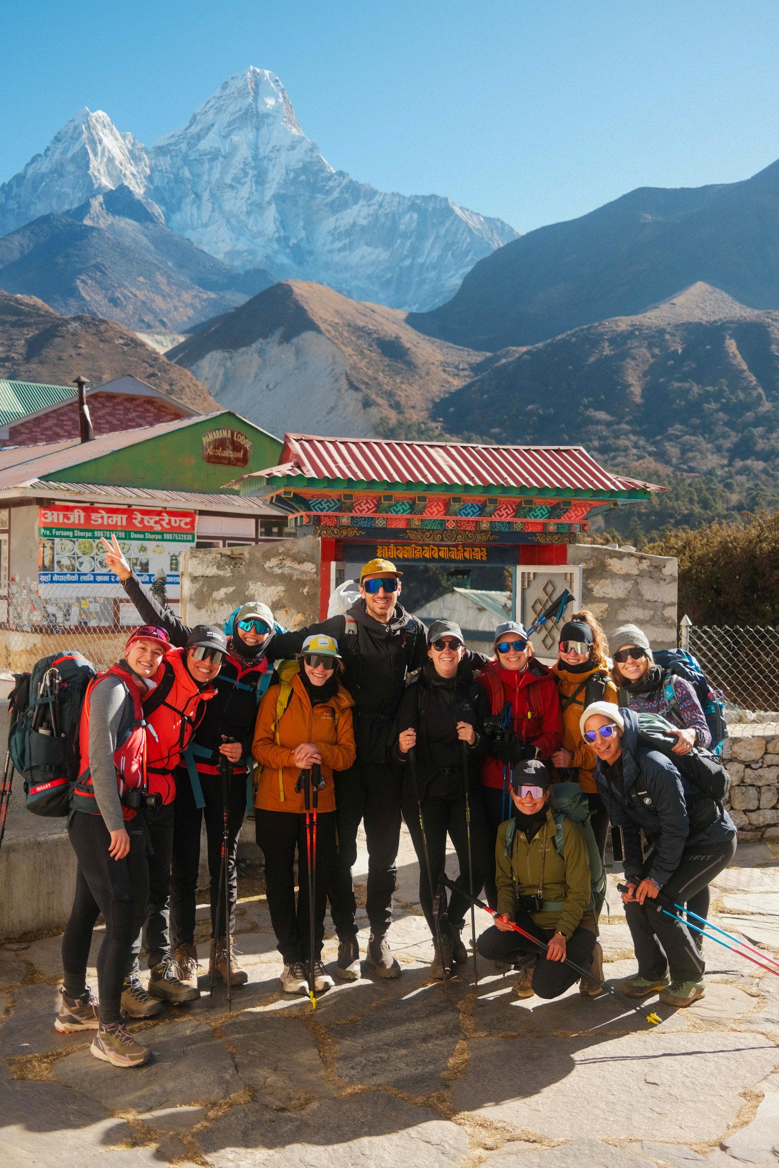 Eine Gruppe von Wanderern in bunten Outfits und mit Rucksäcken vor einer traditionellen asiatischen Tempelanlage mit einem Bergmassiv im Hintergrund.