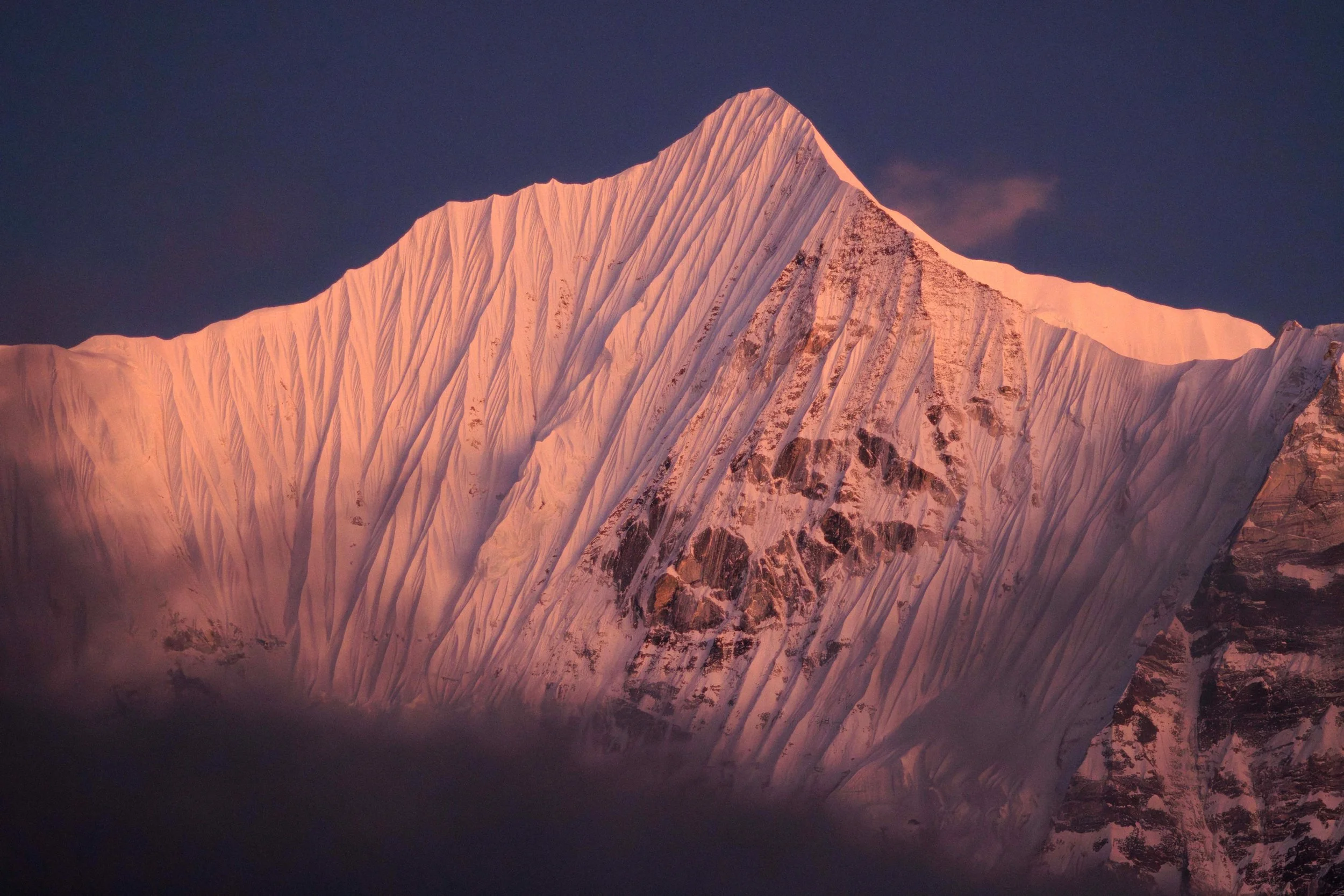 Berggipfel bei Sonnenuntergang, pink gefärbt, mit Schneeflächen und Gletscher, dunkler Himmel im Hintergrund. Abenteuerfotografie erlernen bei Fotografie Workshop mit David Herzig in Nepal. Einzigartige Erlebnisse bei Trekkingreise Himalaya.