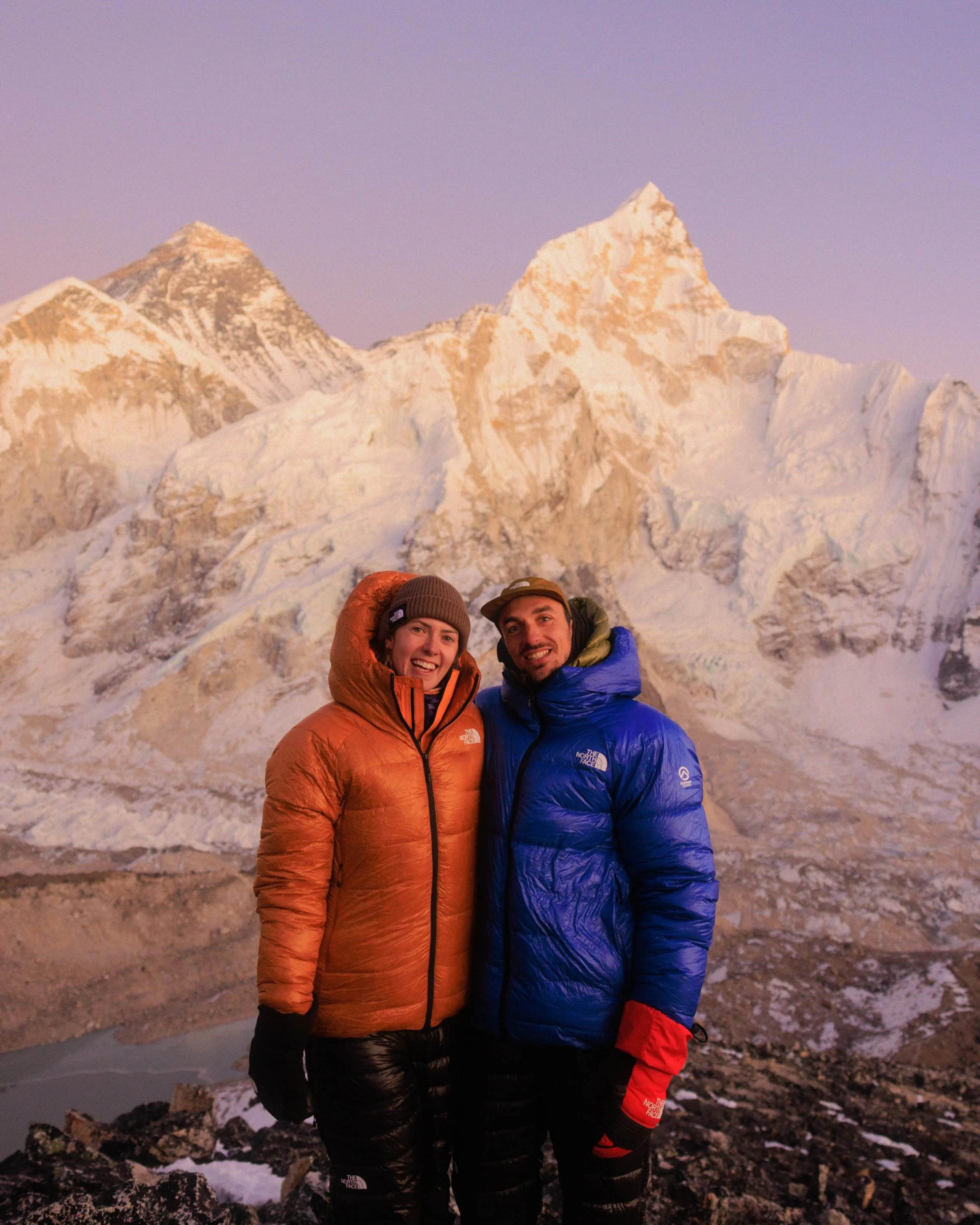 Zwei Menschen in warmer Kleidung vor schneebedeckten Bergen bei Sonnenaufgang oder Sonnenuntergang. Tarah Voss und David Herzig. Reiseleiter mit Herz. Fotografiereise nach Nepal. Trekking und Fotografie Gruppenreise Nepal.