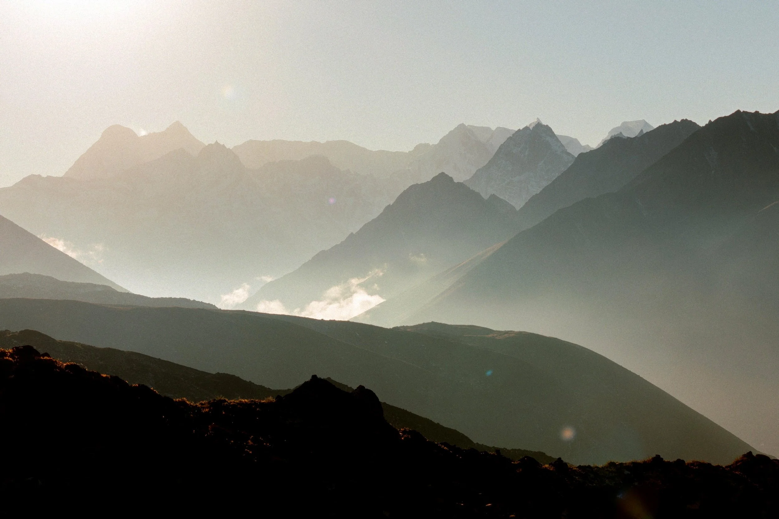 Mehrere Bergketten in der Ferne mit Sonnenlicht, das auf die Gipfel scheint, und wehende Wolken in den Tälern. Freiheit erleben, Energie tanken und Freundschaften knüpfen auf Gruppenreisen mit Aspire Adventures. 
