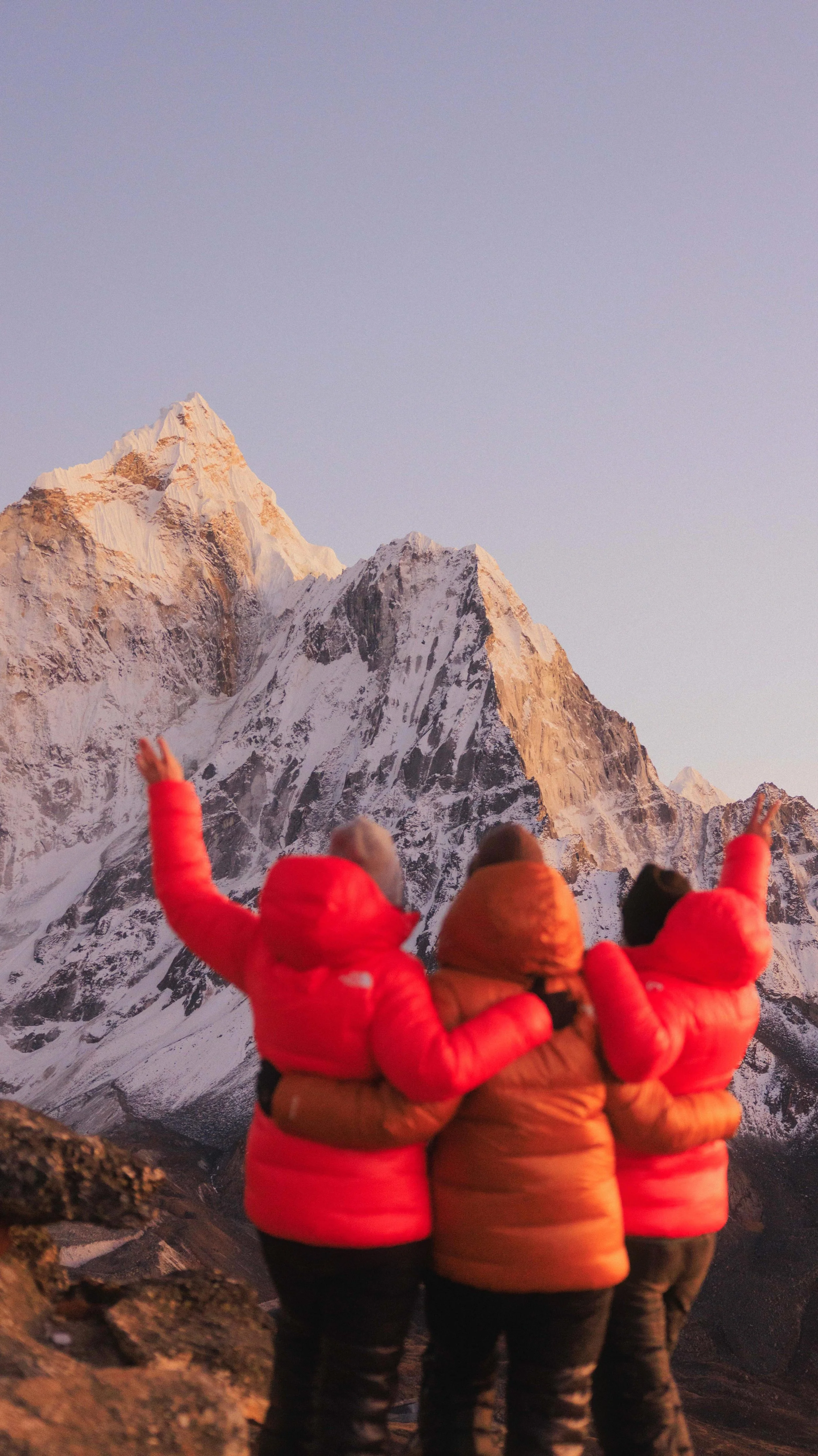 Drei Personen in bunten Jacken, die vor einem verschneiten Berggipfel stehen. Gruppenreise Nepal im Himalaya erleben. Individuelle Gruppenreise zum Everest Base Camp. Gemeinschaft finden und Freundschaften fürs Leben.