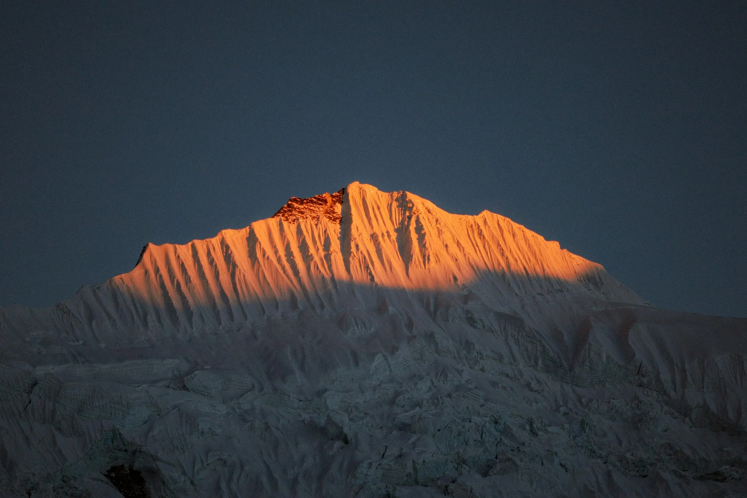 Berggipfel bei Sonnenuntergang mit orangefarbenem Licht auf den Schneeflächen. Trekking und Fotografie Reise Nepal. Gruppenreise zum Everest Base Camp.