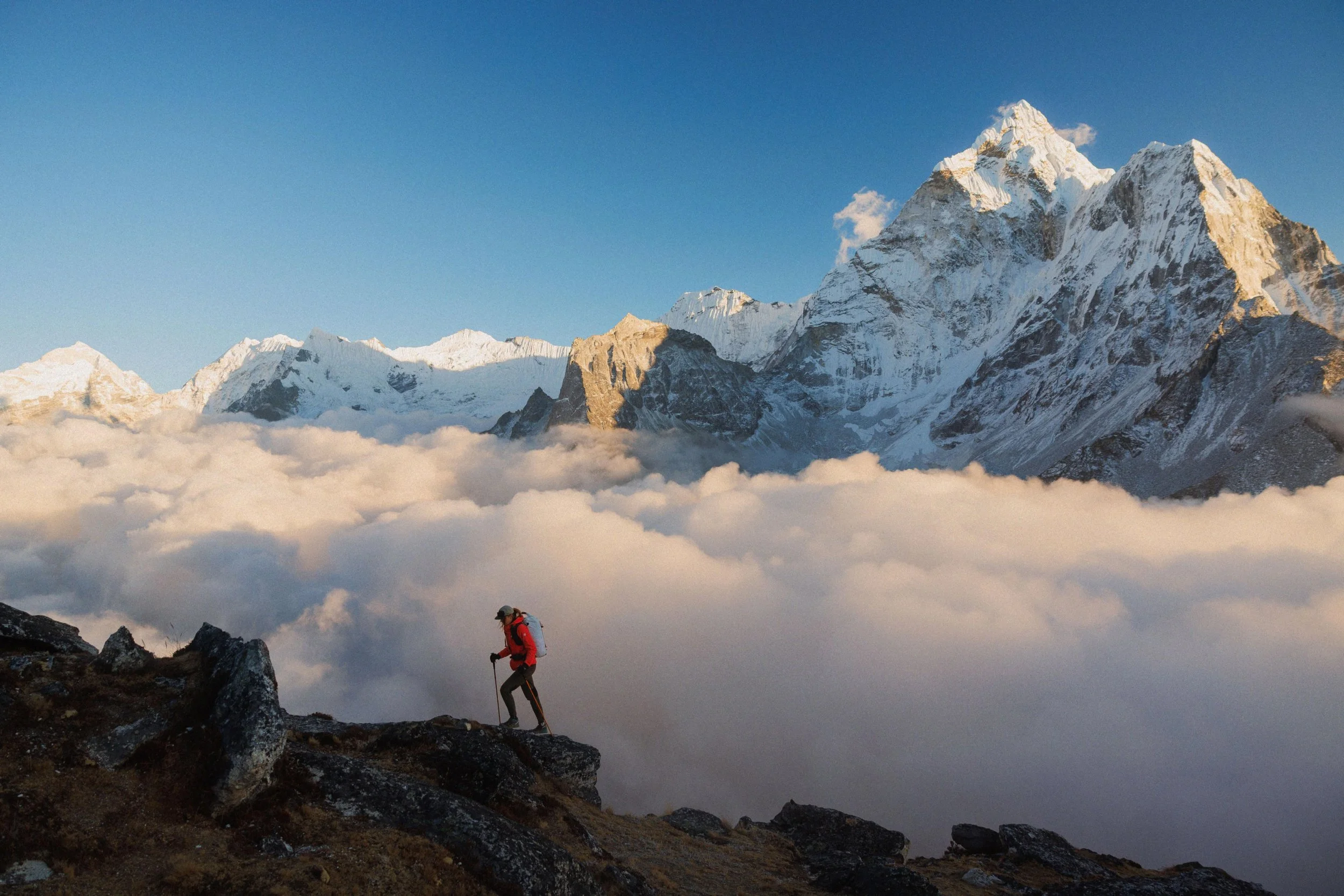 Ein Bergsteiger wandert auf einem Felsen in den Bergen mit schneebedeckten Gipfeln und Wolken im Hintergrund. Himalaya erleben. Trekking Nepal. Trekking Himalaya. Himalaya Reise. Gruppenreise Nepal. Abenteuerreise Nepal. Nepal wandern. Group Trip