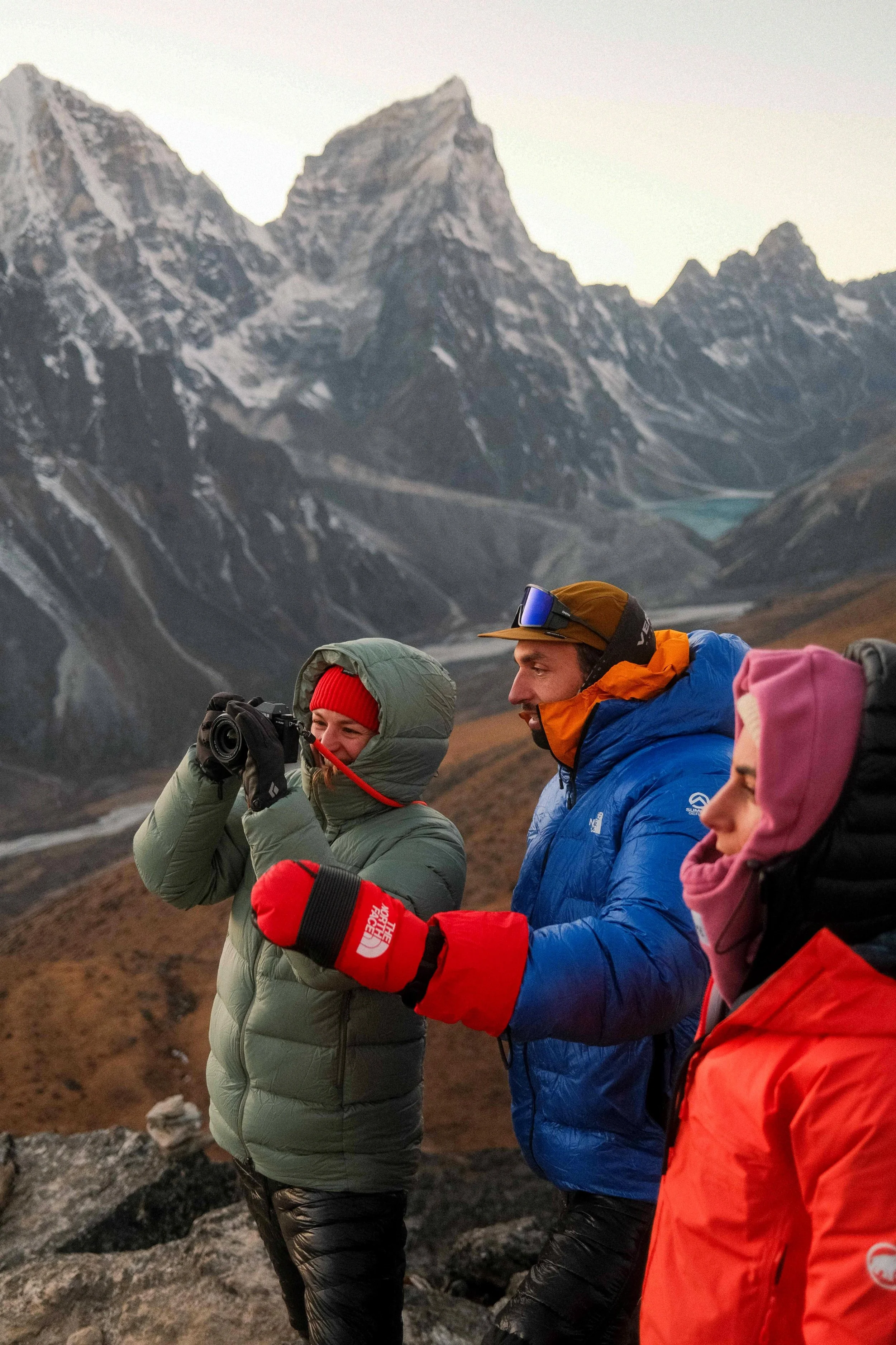 Drei Menschen in wetterfester Outdoor-Kleidung in einer bergigen Landschaft mit hohen, schroffen Bergen im Hintergrund. Einer der Männer zeigt auf etwas, während die anderen zuschauen.
