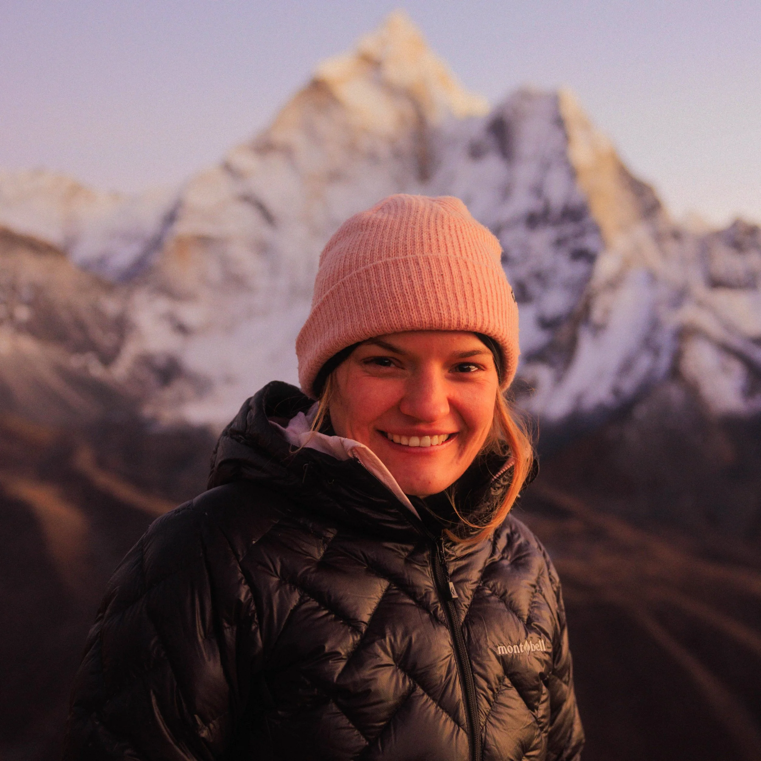Junge Frau in Winterkleidung vor schneebedecktem Berg in den Bergen bei Sonnenuntergang.
