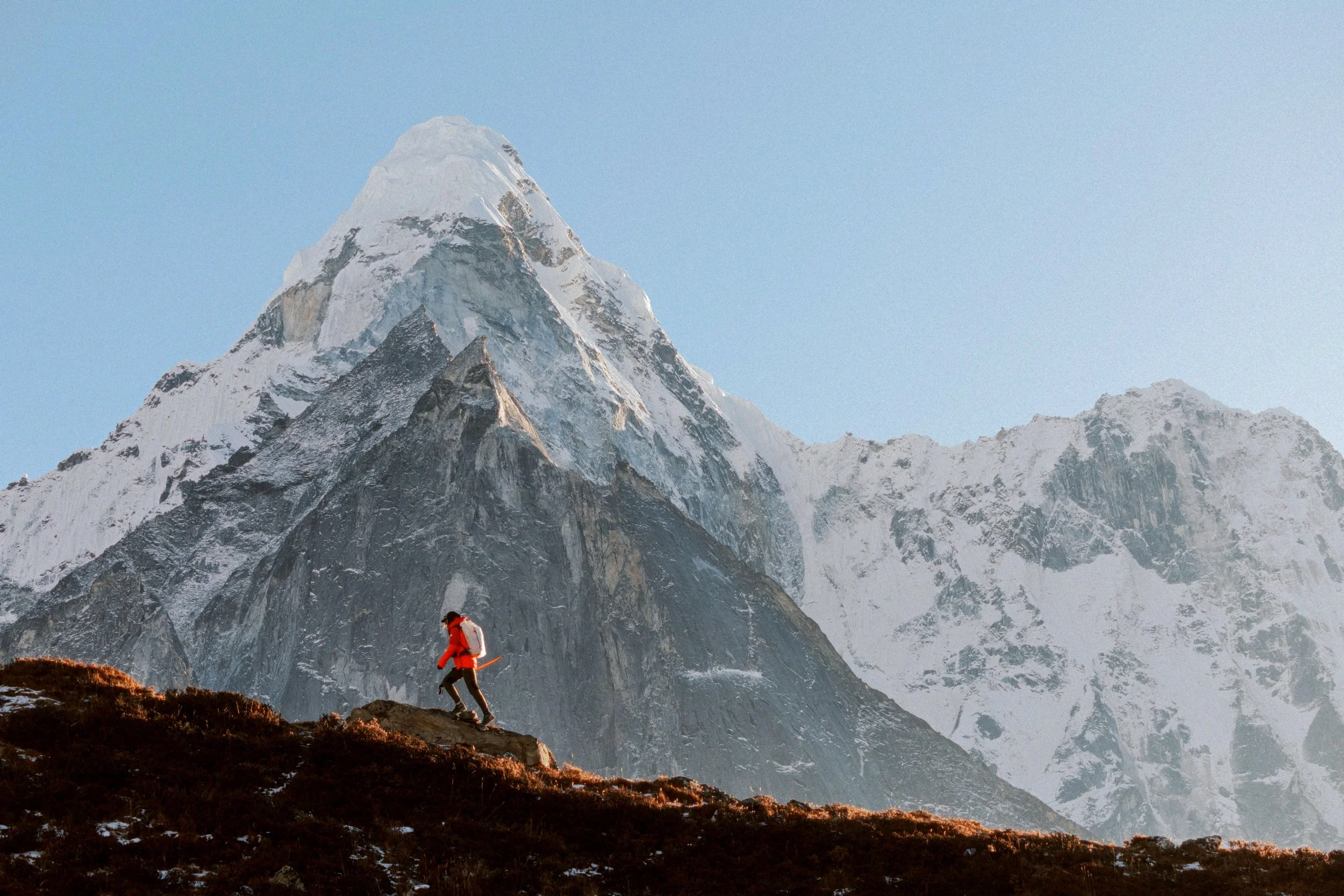 Eine Bergsteigerin in roter Jacke auf einem Felsen vor einer schneebedeckten Bergkette im Himalaya. Trekkingreise Nepal erleben in gleichgesinnter Gruppe. 