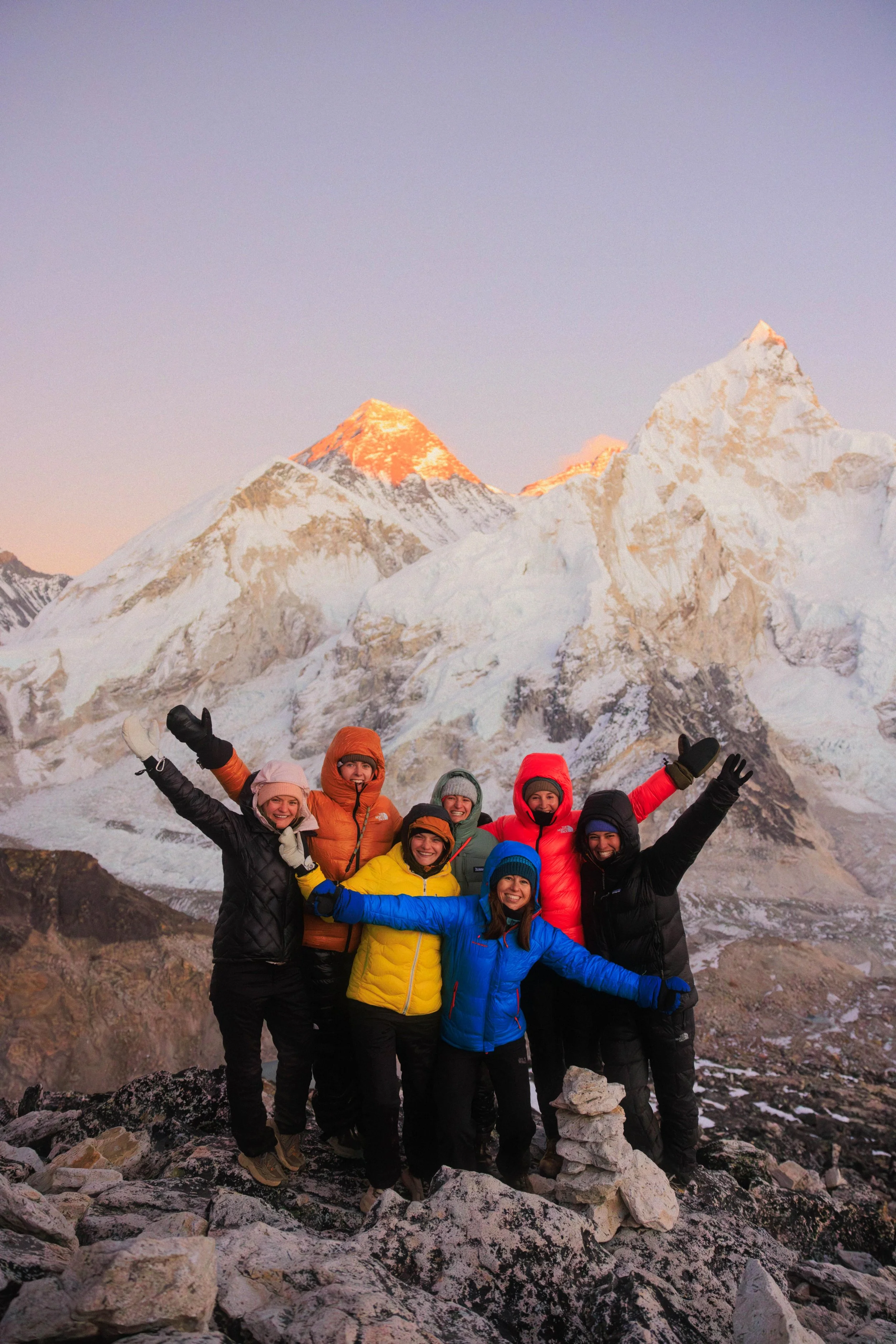 Eine Gruppe von acht Menschen in Winterkleidung freut sich vor einer schneebedeckten Bergkulisse, vermutlich im Himalaya.