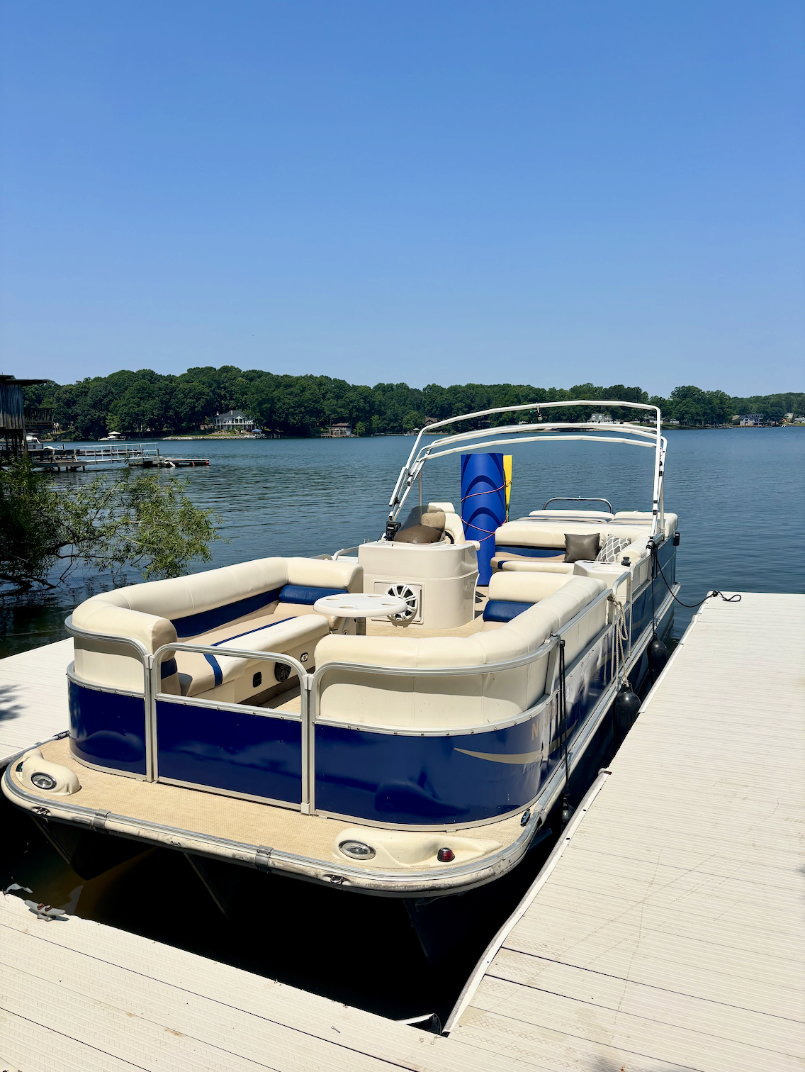 A pontoon boat docked on Lake Norman on a clear, sunny day with calm water and green trees in the background.