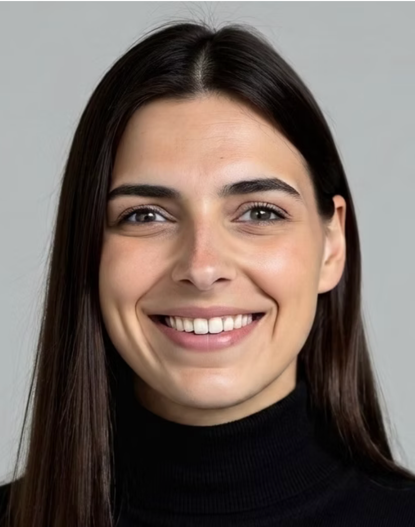 A young woman with long dark brown hair, smiling and showing her teeth, wearing a black turtleneck, against a plain gray background.
