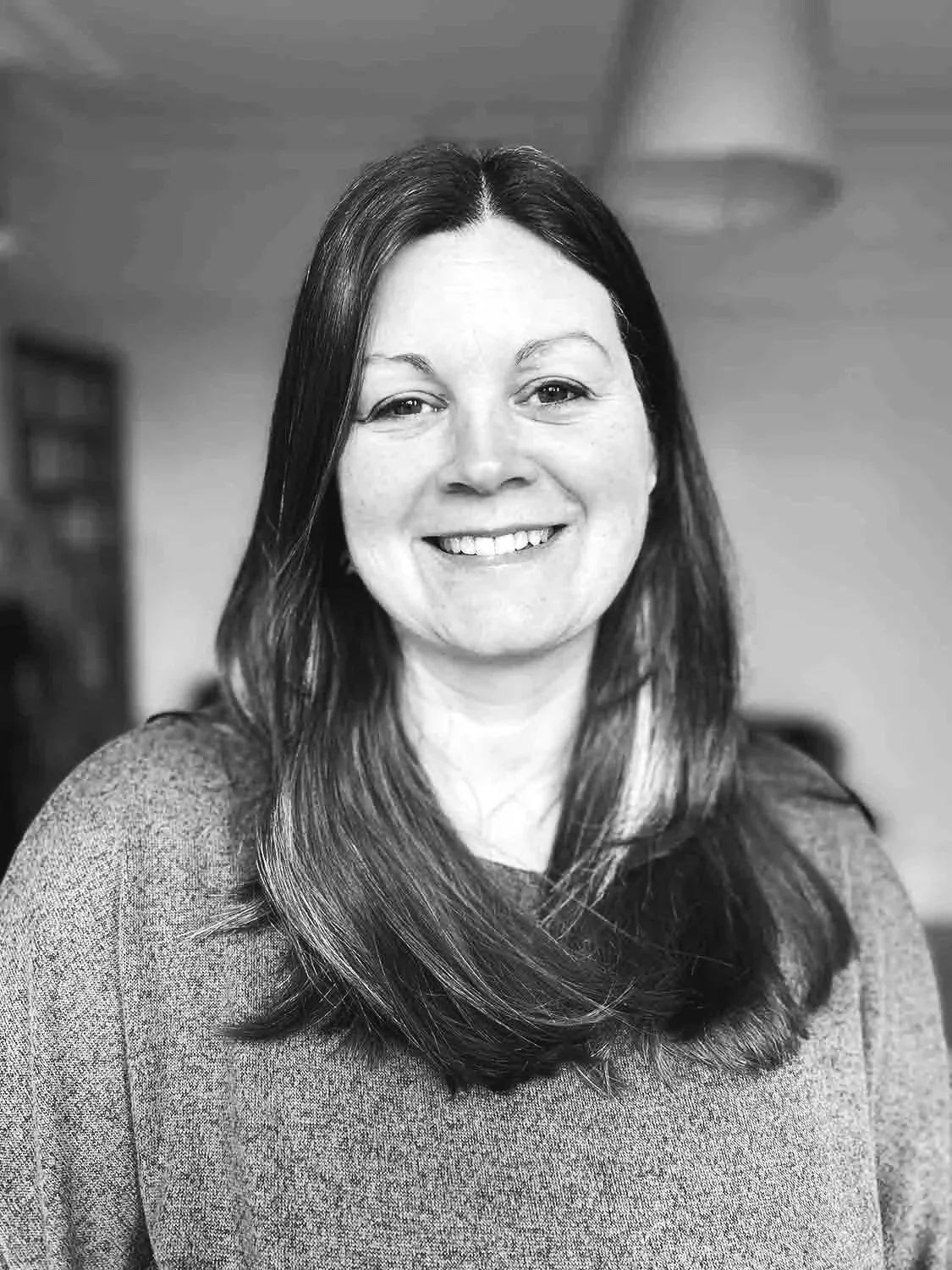 Black and white portrait of a woman with long dark hair, smiling, wearing a sweater, indoors.