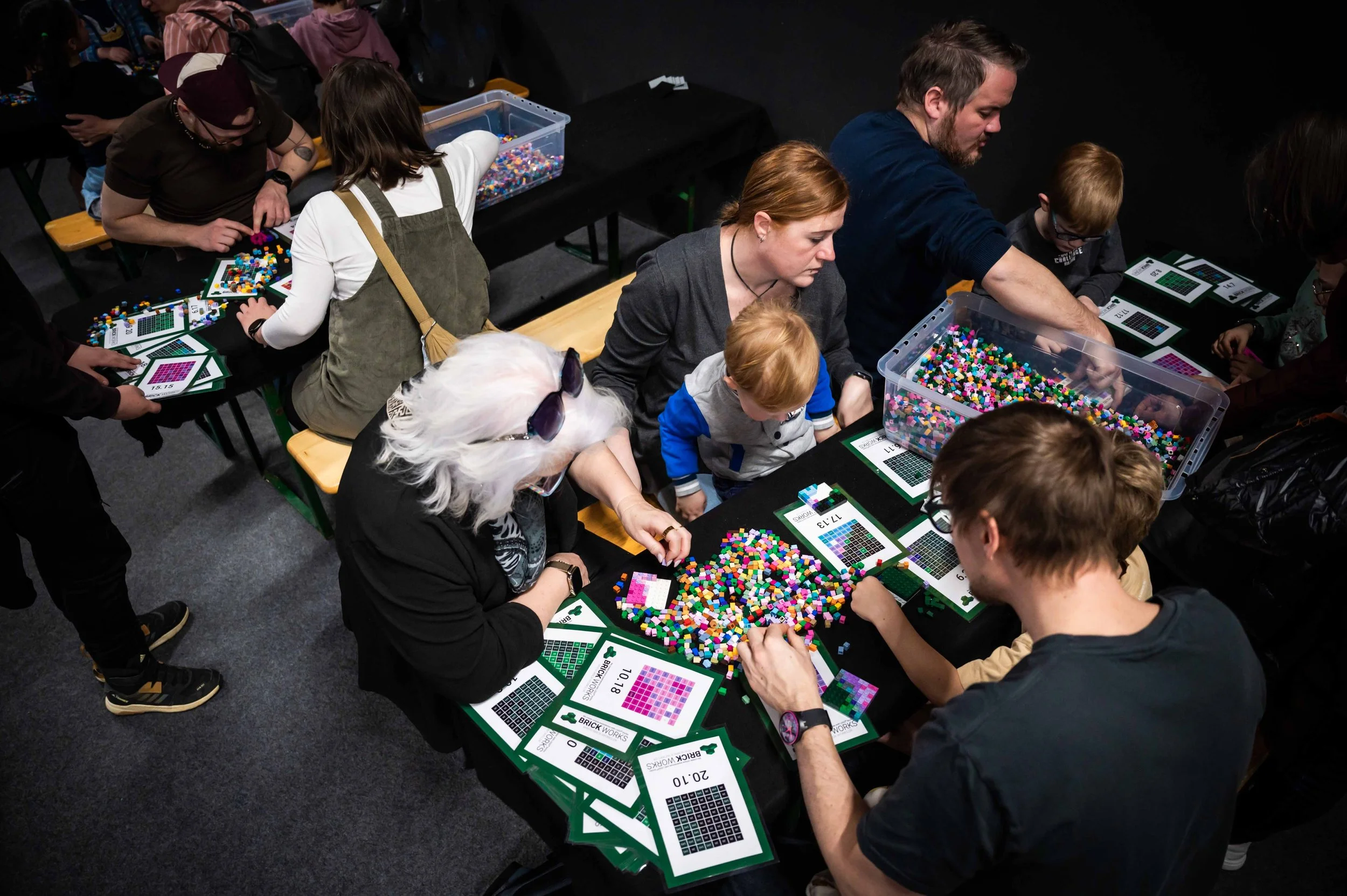 Menschen beim Lego-Muster bauten in einem Raum, mit Tischen, Lego-Steinen, Anleitungskarten und Werkzeugen.