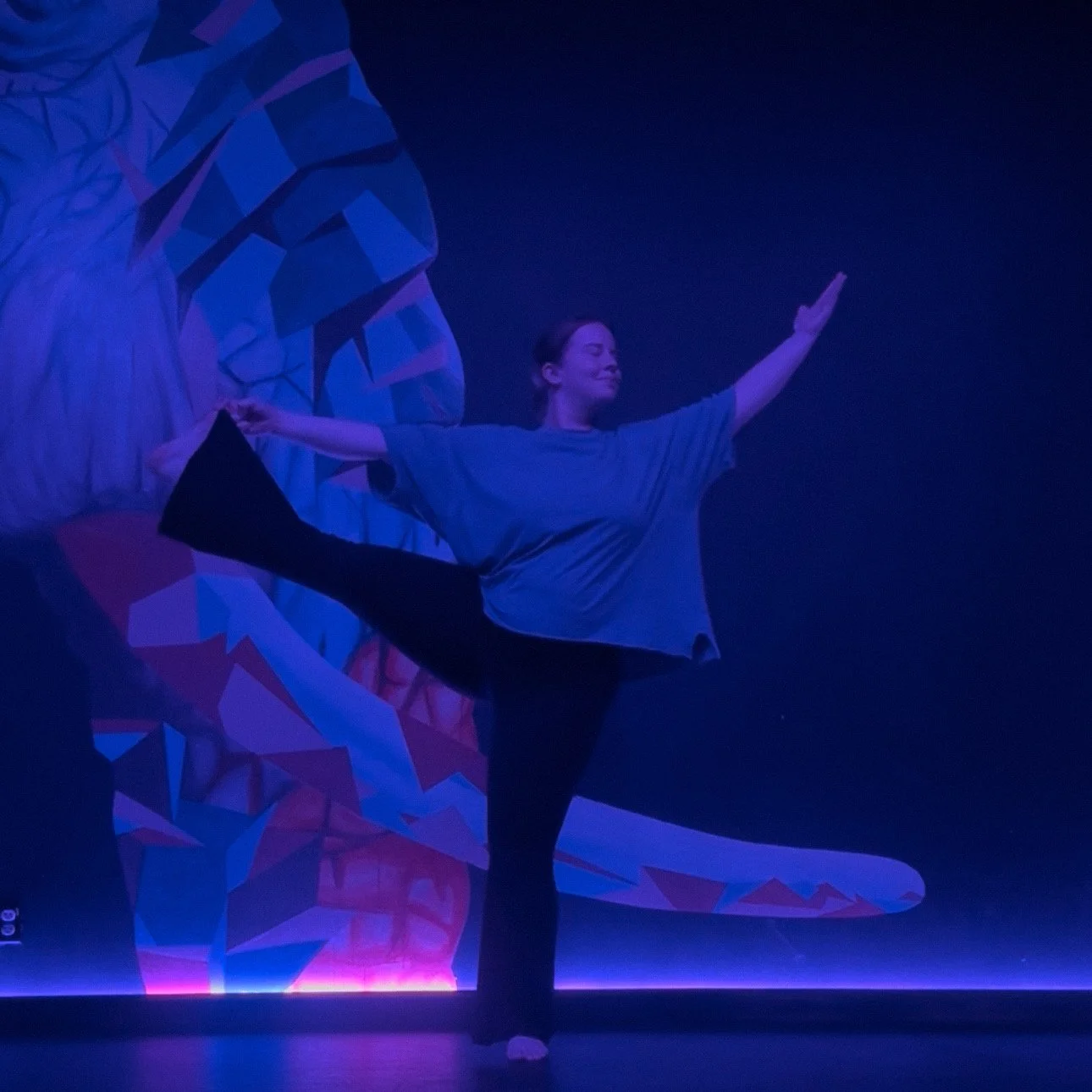 Woman practicing yoga on stage with colorful abstract background under purple lighting