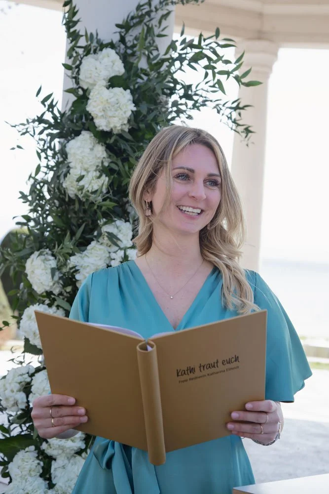 Die freie Rednerin in einem blauen Kleid steht mit einem Buch in der Hand und wirkt entspannt.