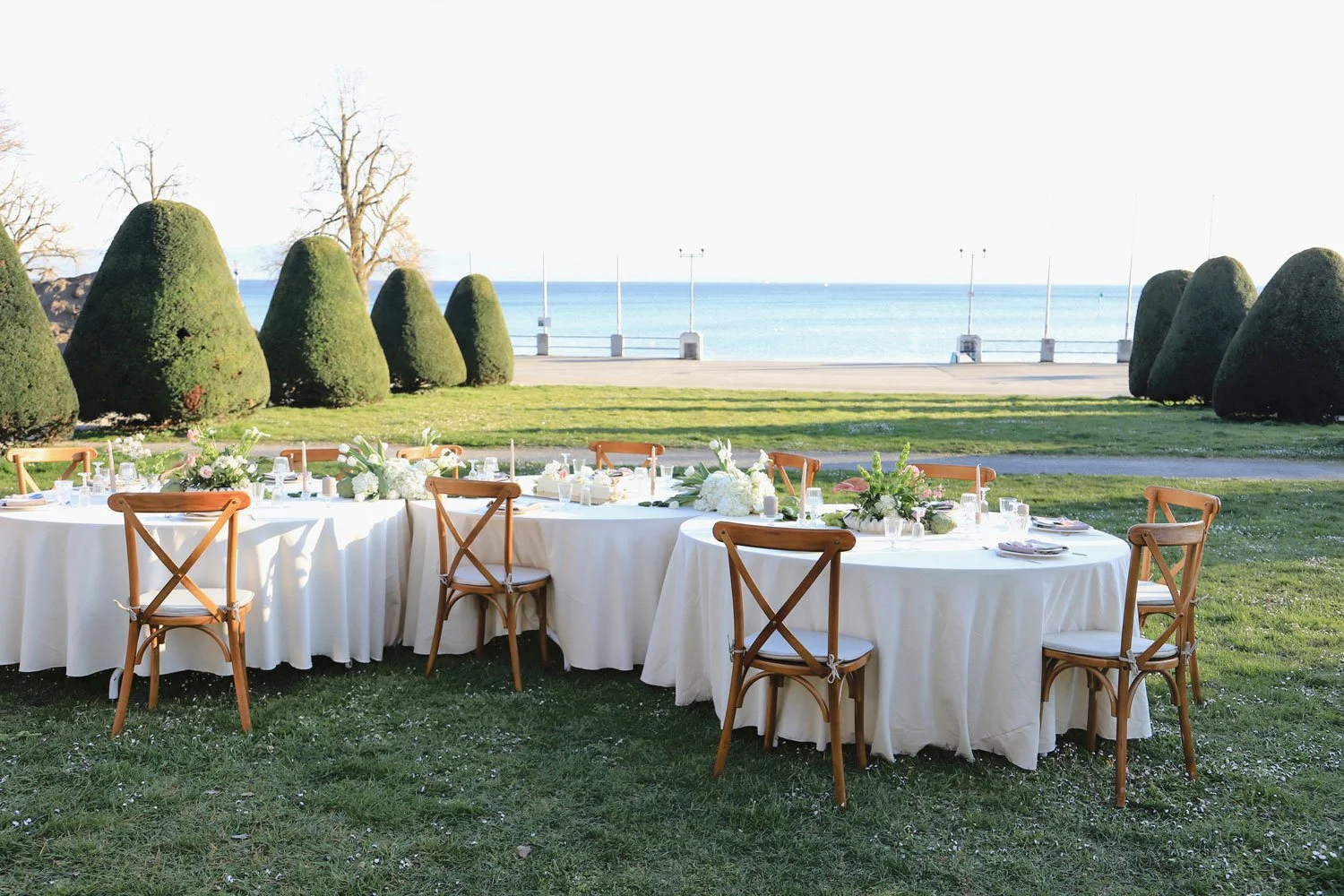 Ein festlich gedeckter Tisch für eine Hochzeitsfeier auf grünem Gras, umgeben von Blumen und Dekorationen.