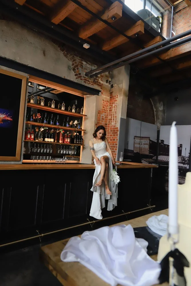 Eine Braut in einem eleganten Hochzeitskleid sitzt an der Bar und genießt den Moment.