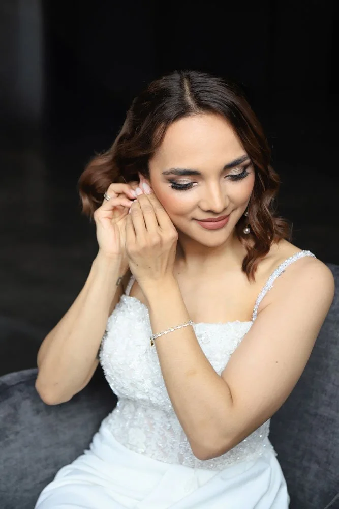 Die Braut in einem weißen Kleid legt ihre Ohrringe an.