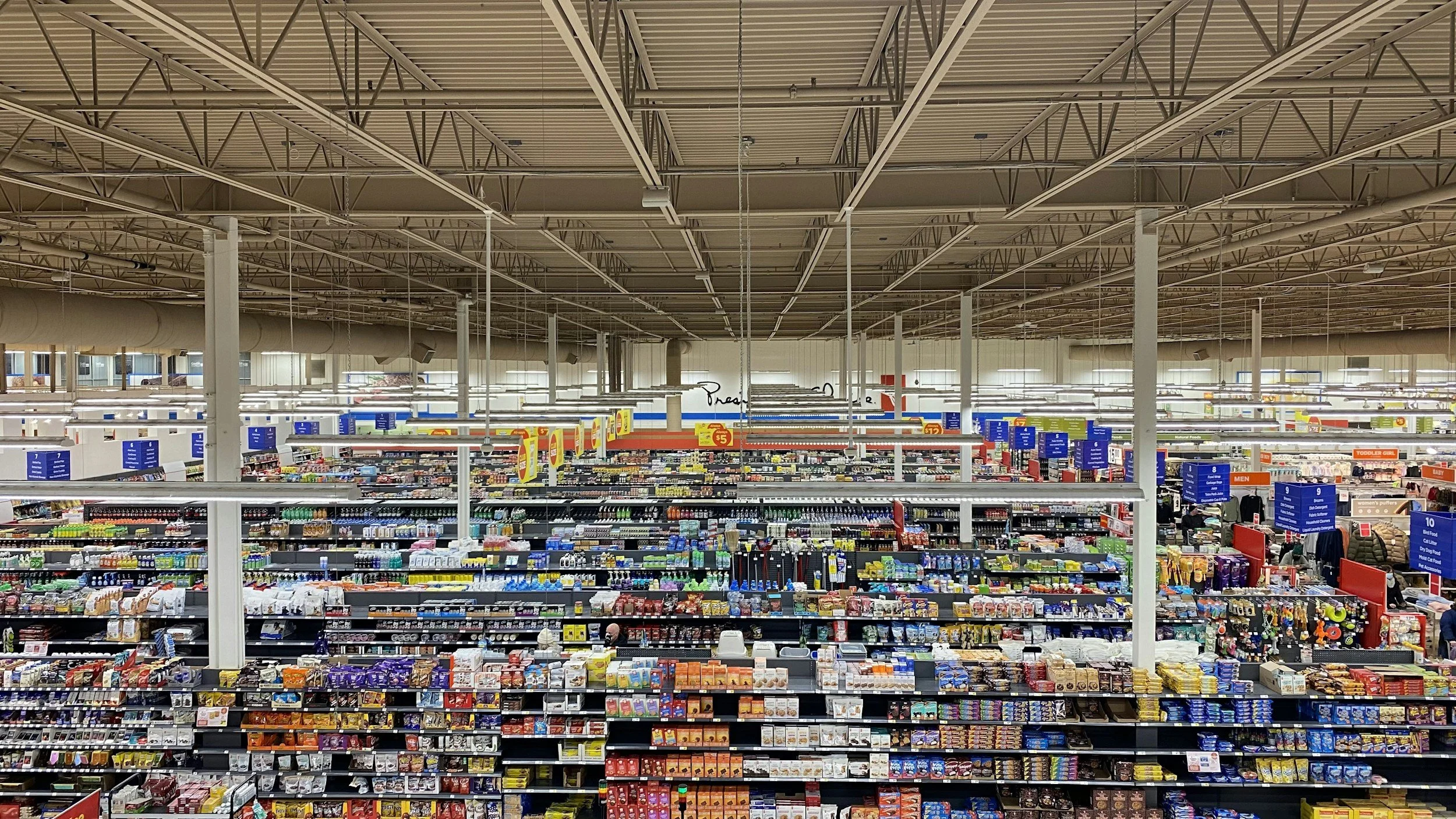 Interior of a large grocery store with aisles stocked with various packaged goods and blue signage overhead.