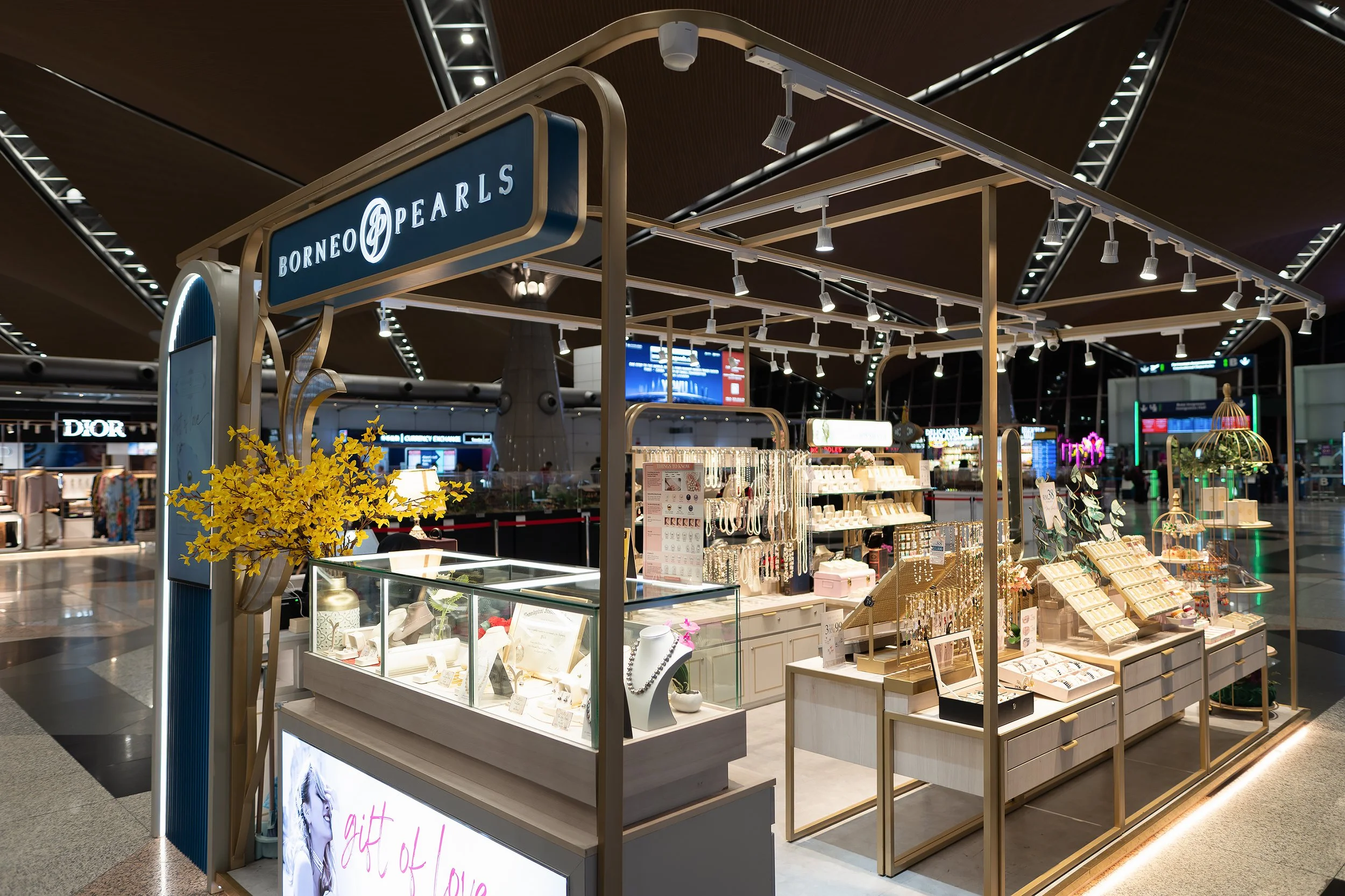 Jewelry kiosk at airport with display cases, jewelry and accessories, and a sign that reads 'Borneo Pearls' in an airport terminal.